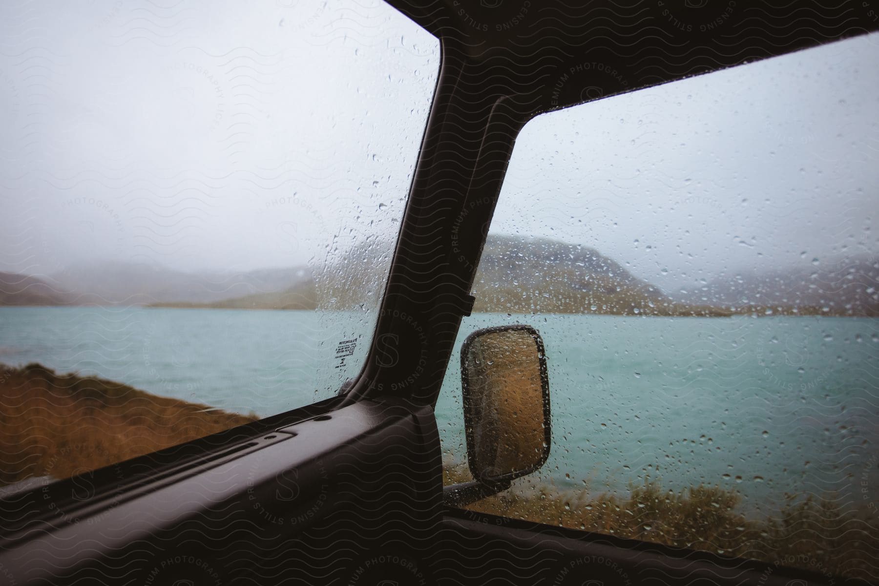 A car door provides a view of a body of water and a hill in the background