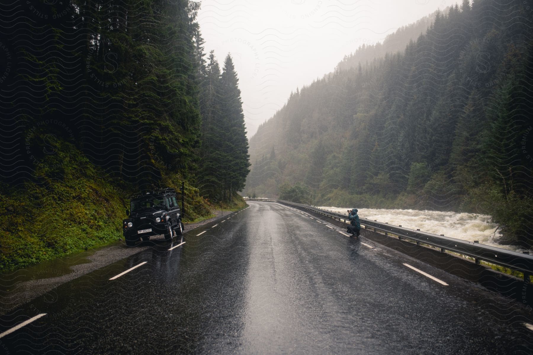 A man photographing his car in a forest with a tiled road