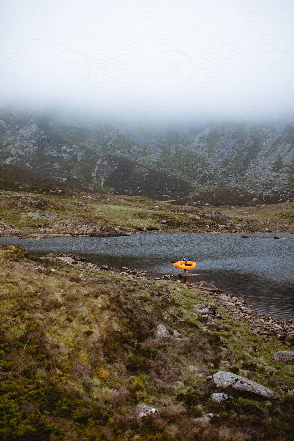 A man holding a canoe on a lake surrounded by rocky mountains