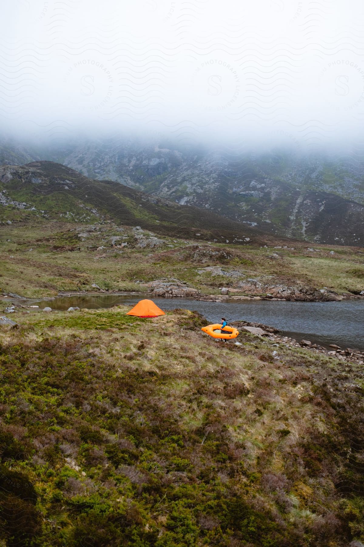 A man camping in the hills near a lake carrying an inflatable boat to his tent