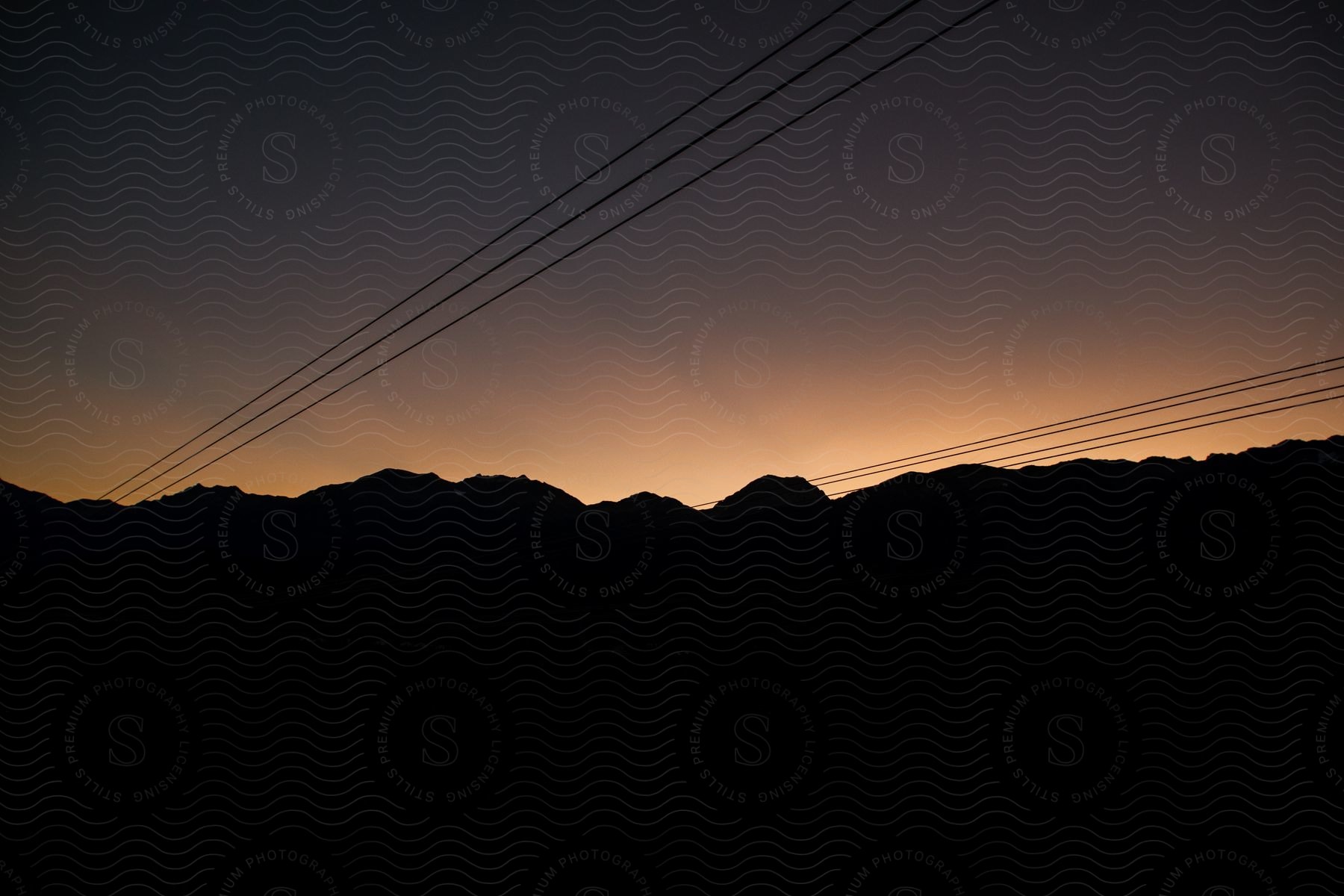 Sun setting over horizon with pink sky turning darker over silhouetted power lines and trees