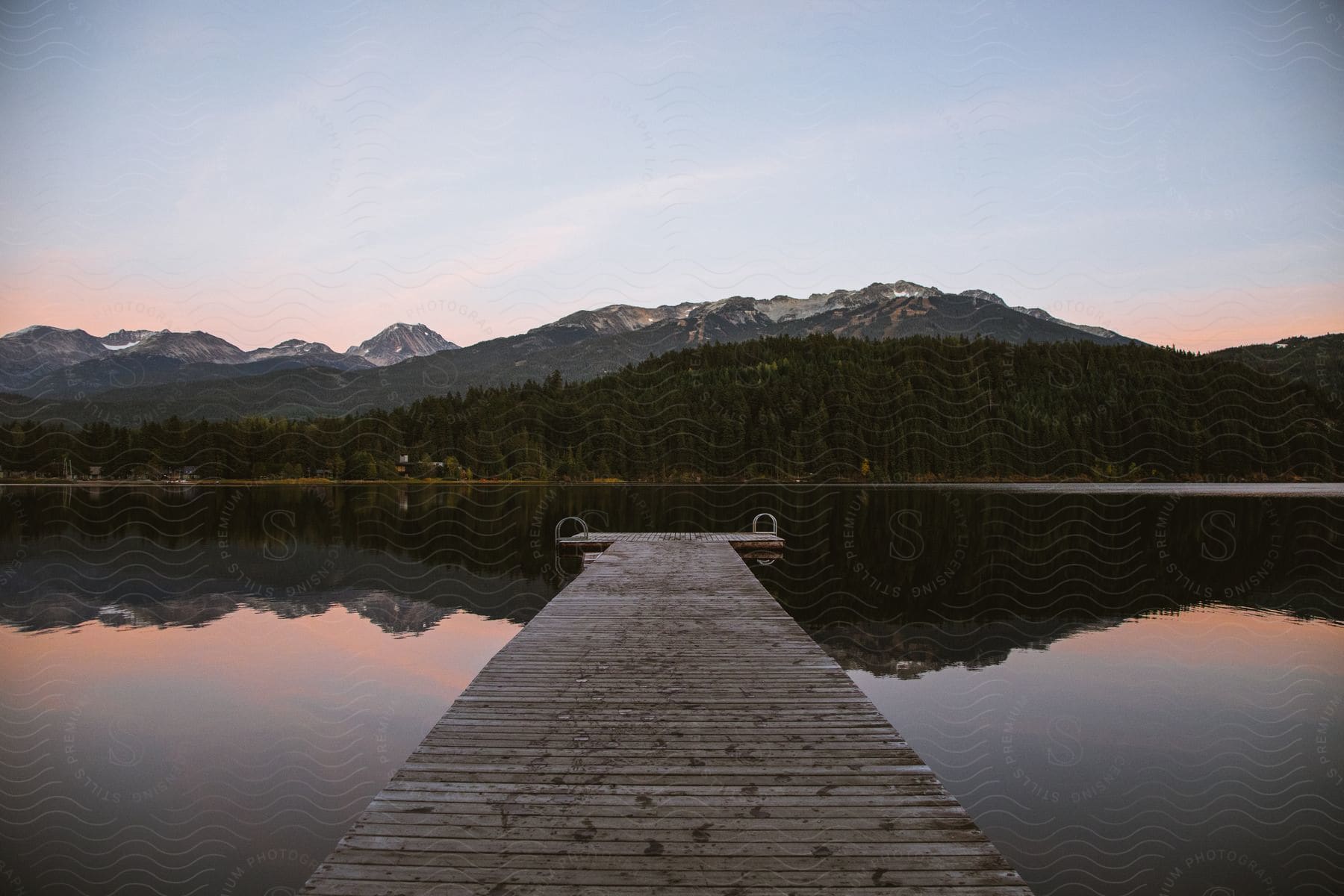 Wooden dock stretching into a lake with mountains and a forest on the other side