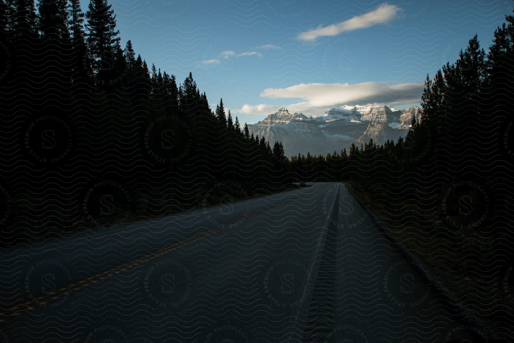 A winding twolane road cuts through a forest with mountains in the background