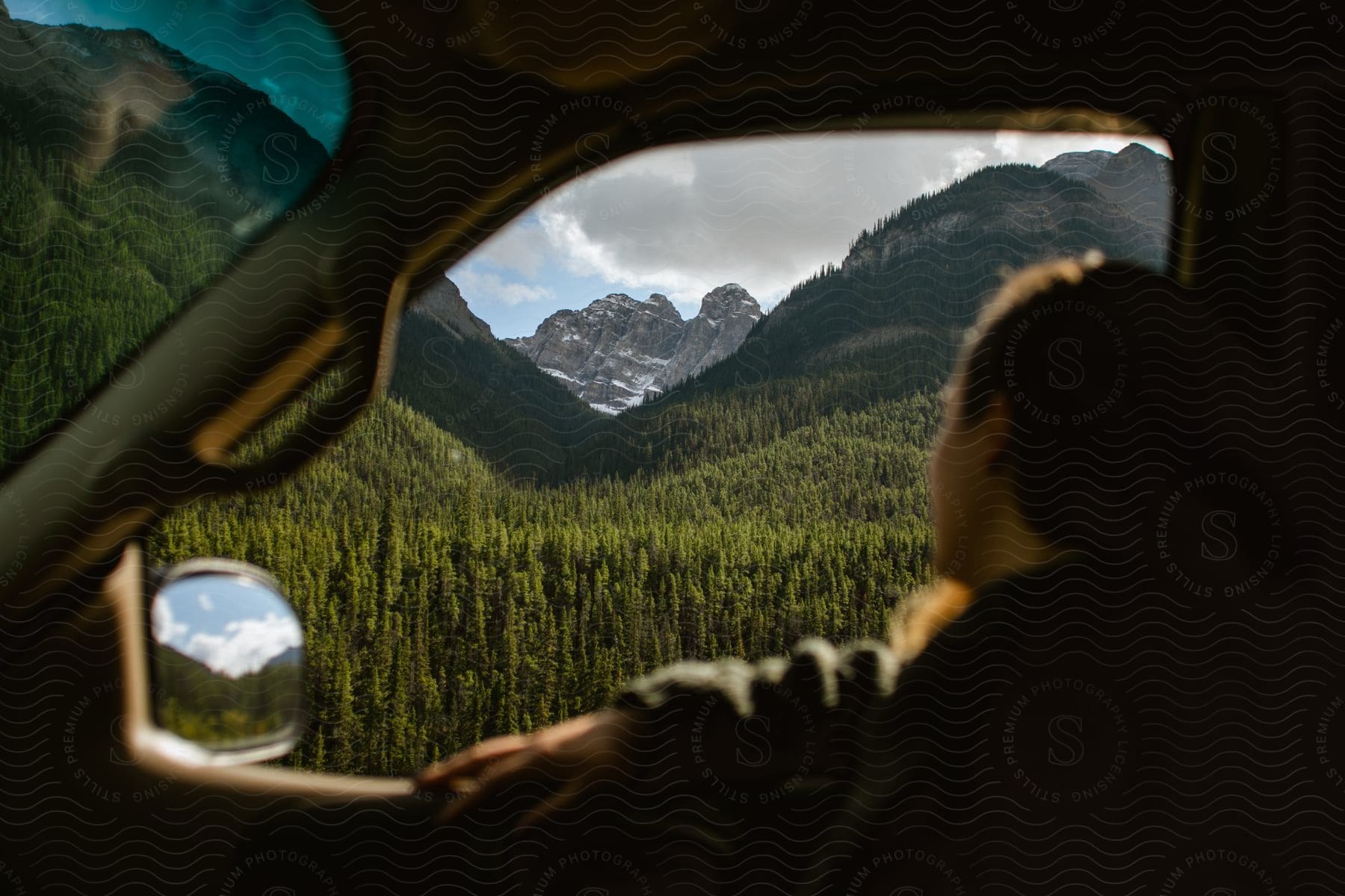 A man looks out the car window at a mountain range with forest