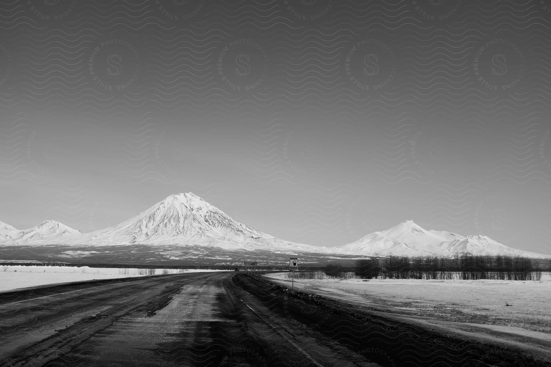 Snow melts on a blacktop road near a mountain range