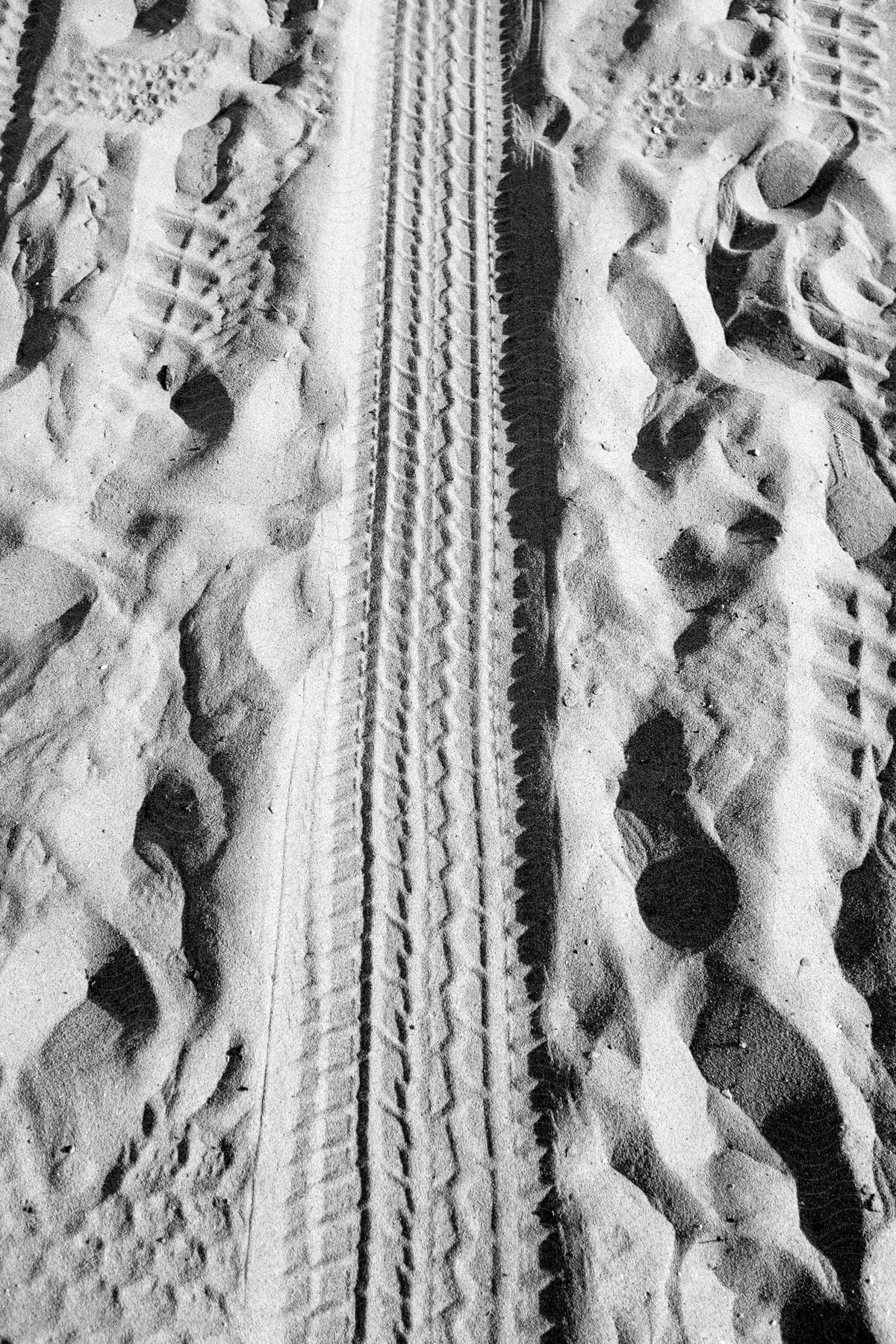 Tire tracks crisscross with shoe prints on a sandy shoreline