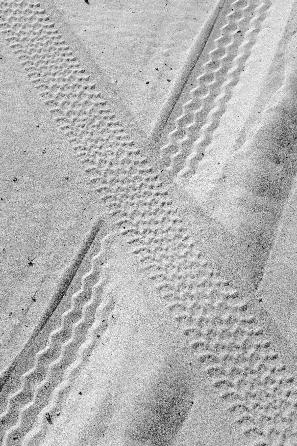 Tire tracks crisscross on white sand during the day