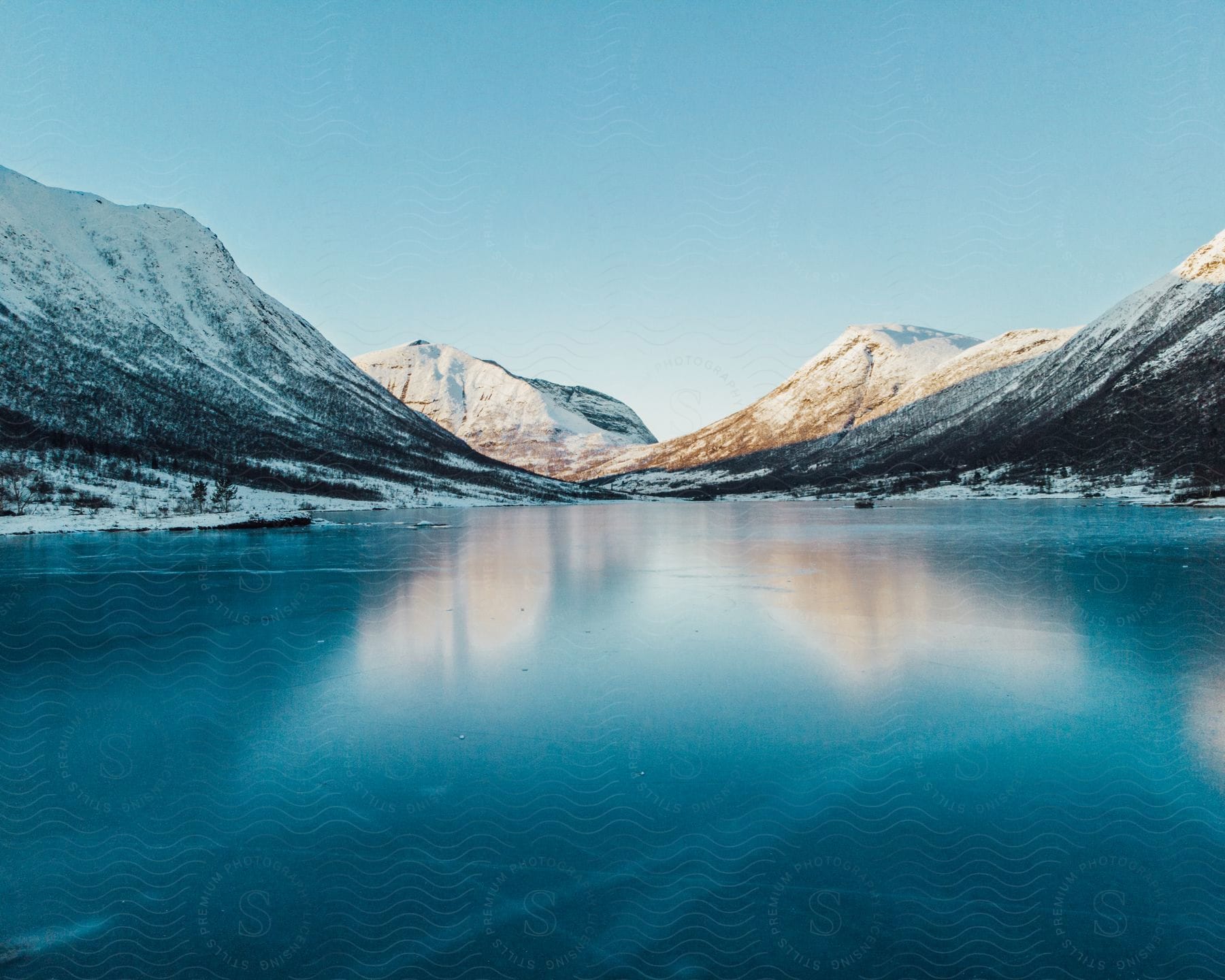 A serene winter landscape with a frozen lake surrounded by mountains and snow