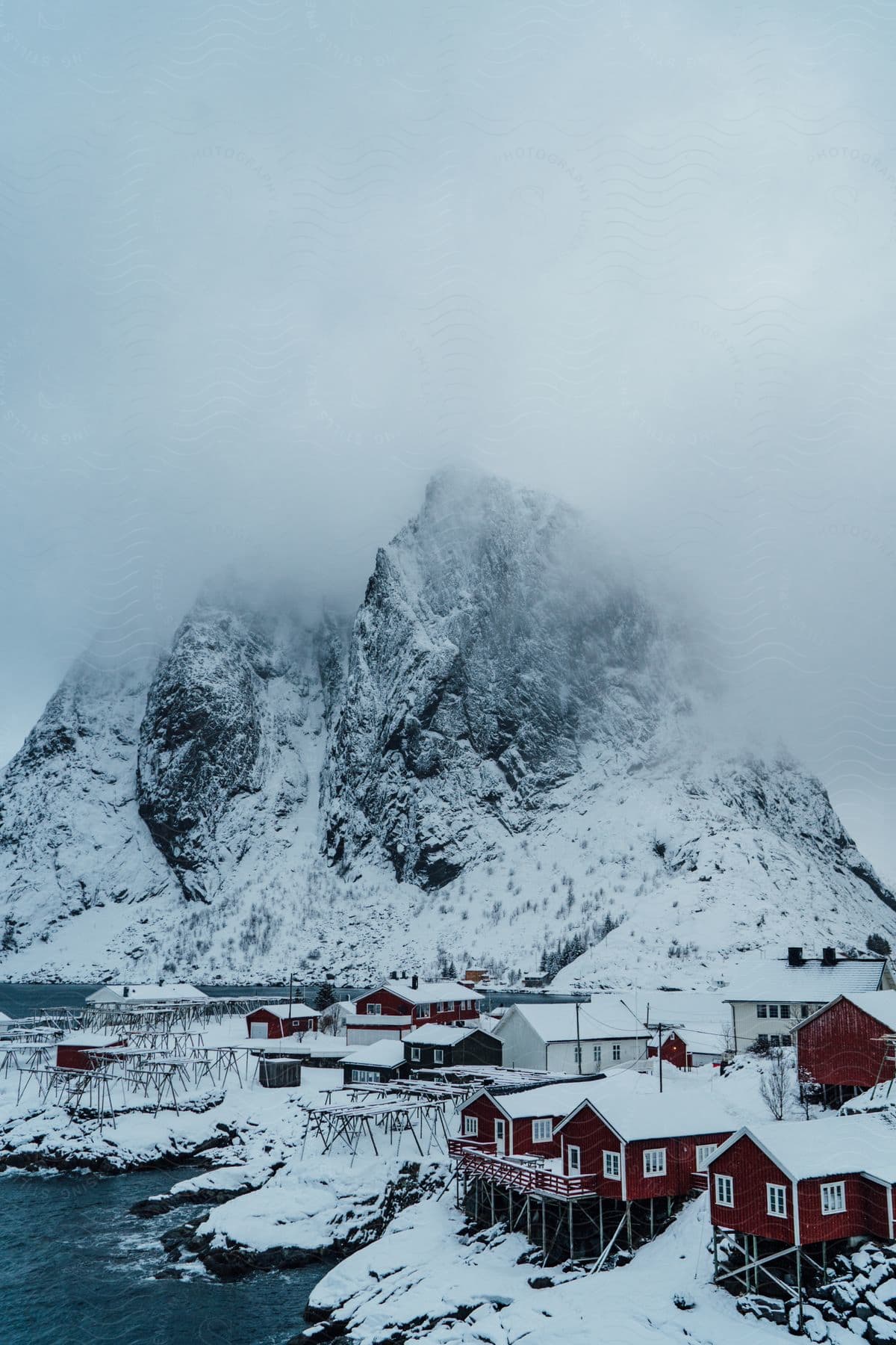 A snowy small town by the coast is seen with a foggy mountain backdrop