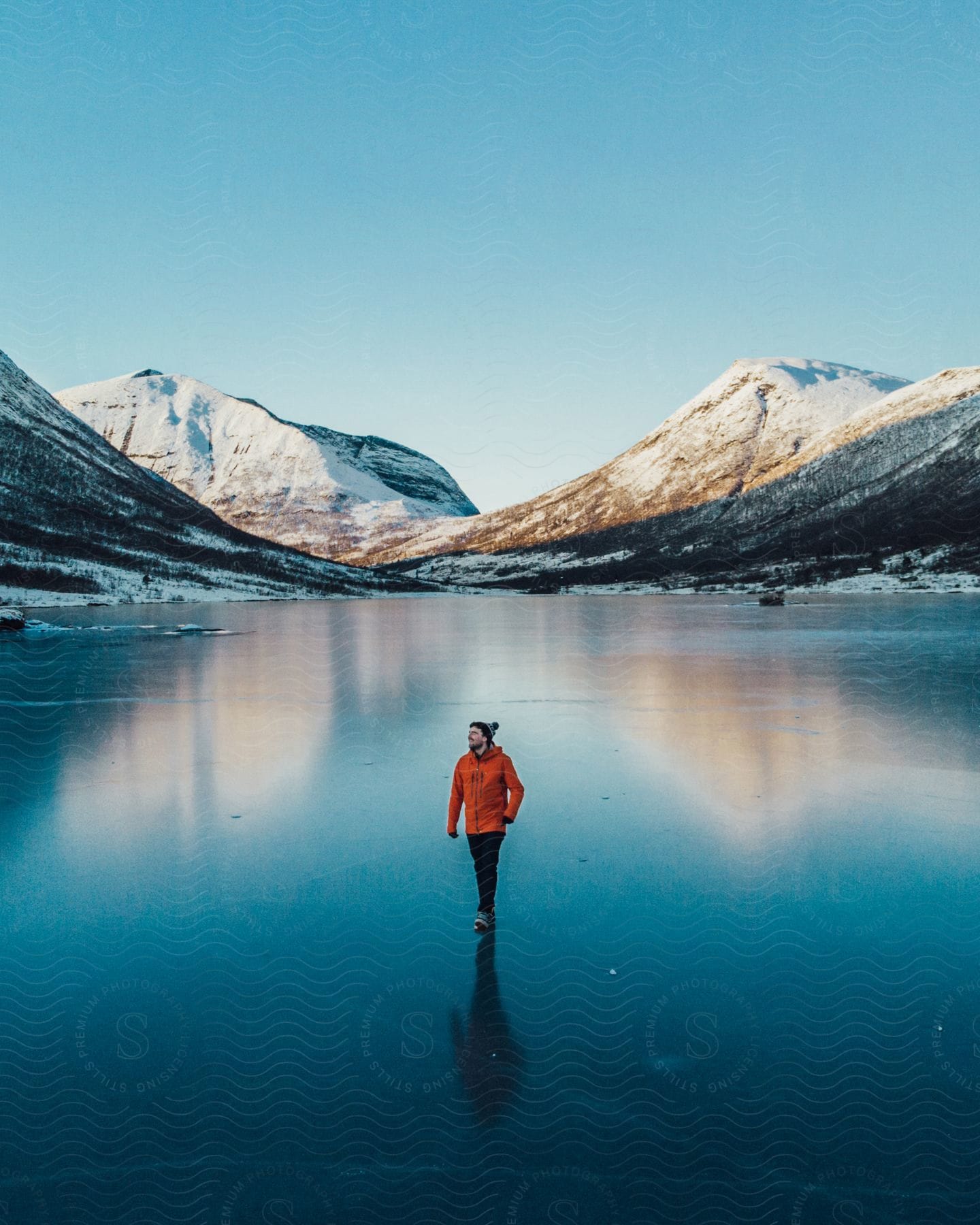 Man walks across frozen lake with snowy mountains in the background.