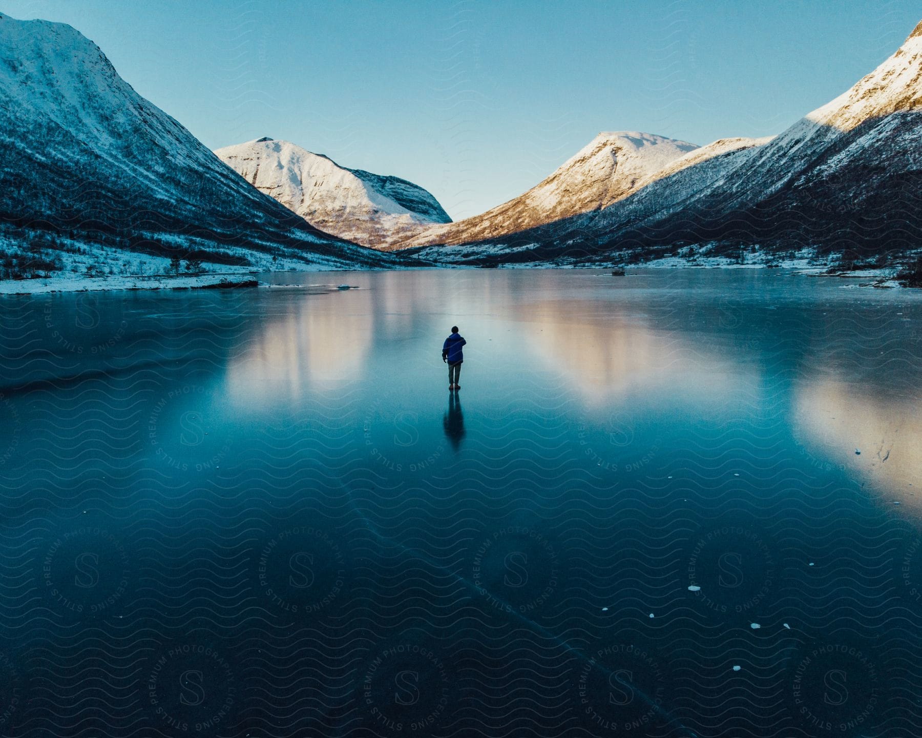 A man captures a photo near mountains on a frozen lake in norway