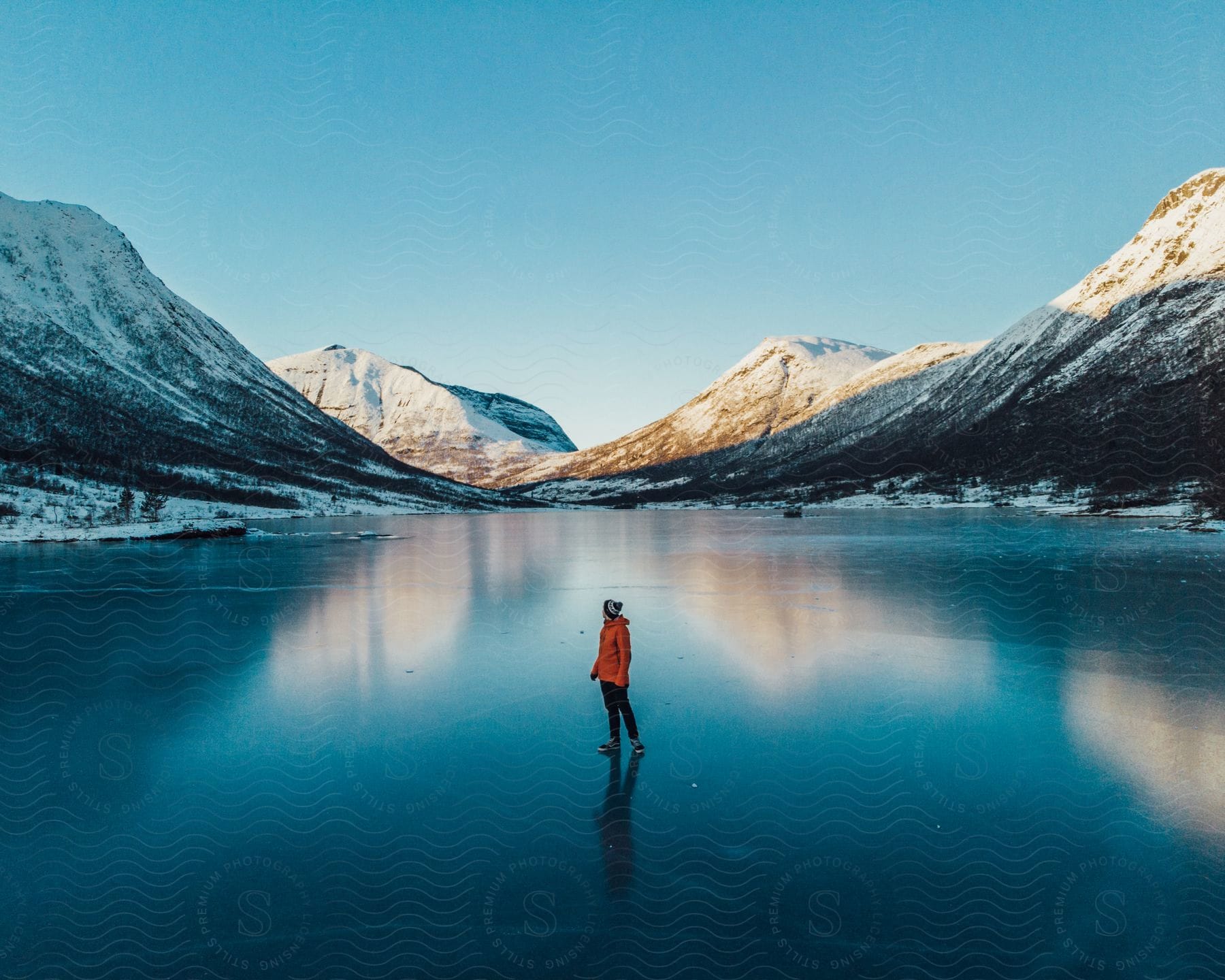 A person stands on a frozen lake with snowy hilltops around them in norway