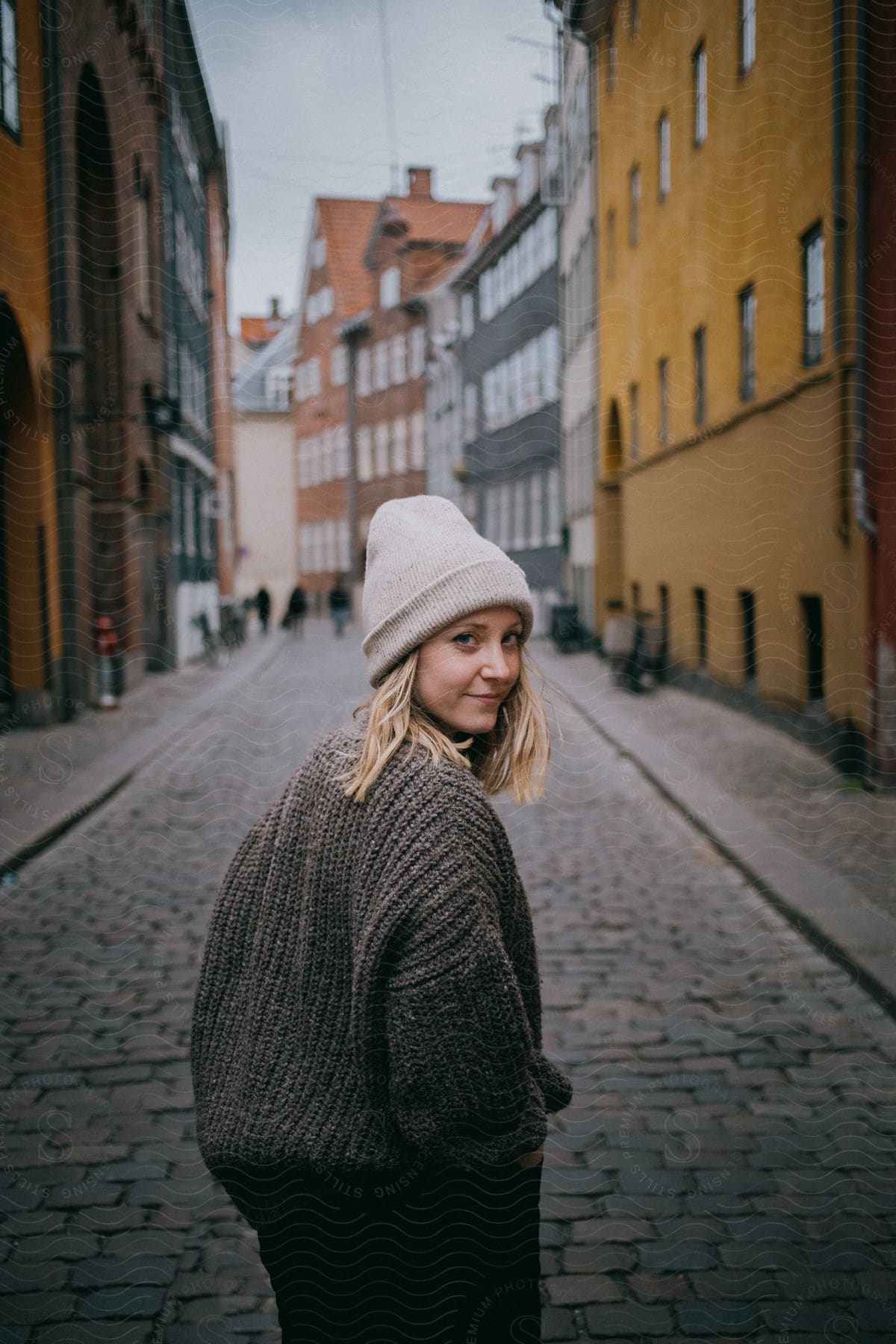 A woman is walking on an alley with buildings close together as she looks back and smiles