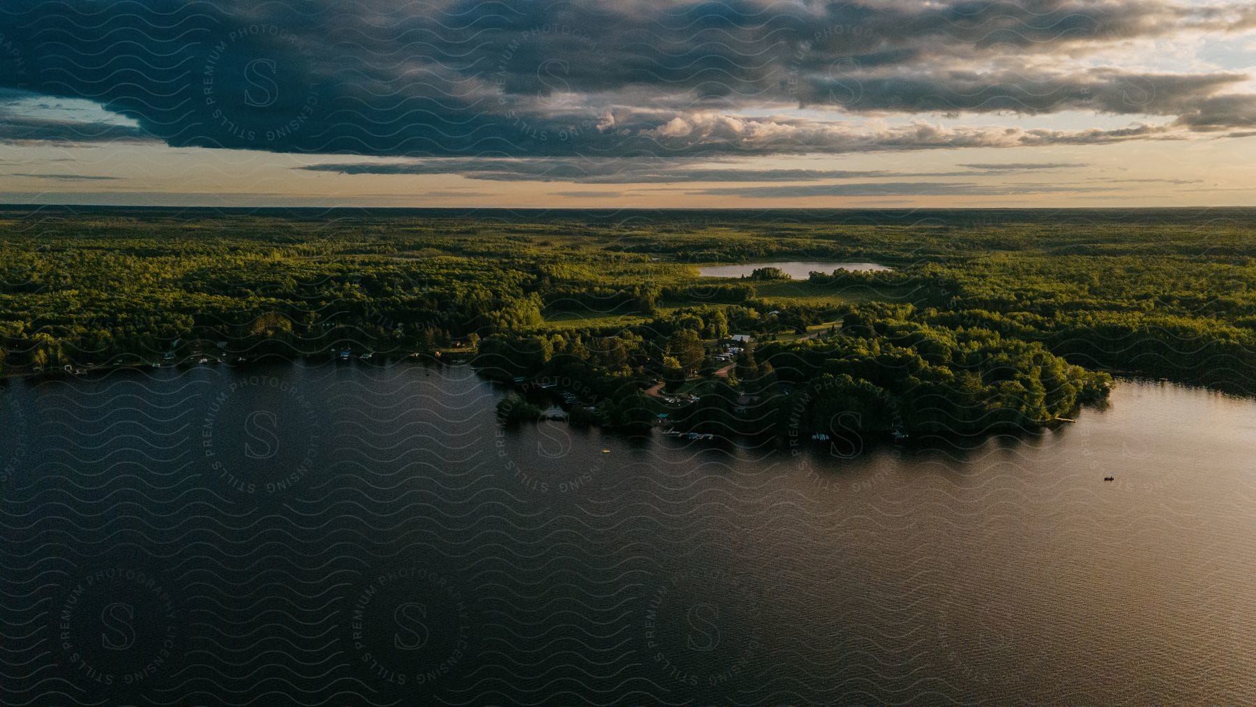 Aerial shot of a lake surrounded by forests of trees and a cloudy light gray sky at dusk in wisconsin north woods