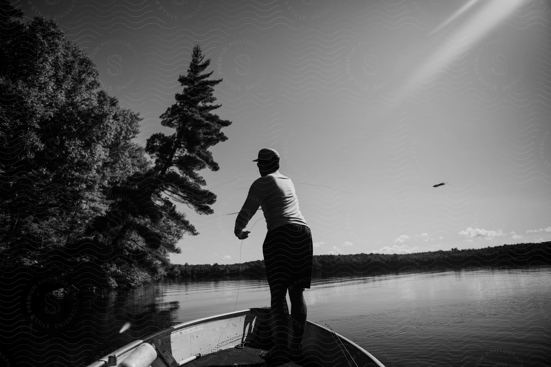 A man stands on a boat on a lake and uses a fishing rod