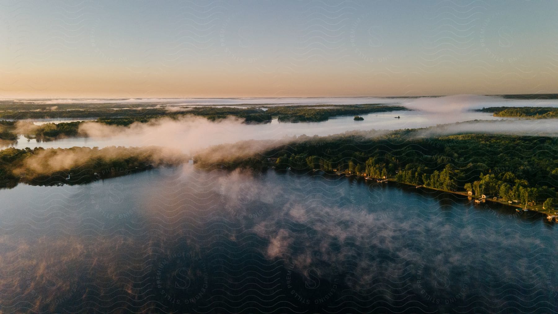 Fog partially covers trees near the shoreline of a river at sunrise in the wisconsin north woods