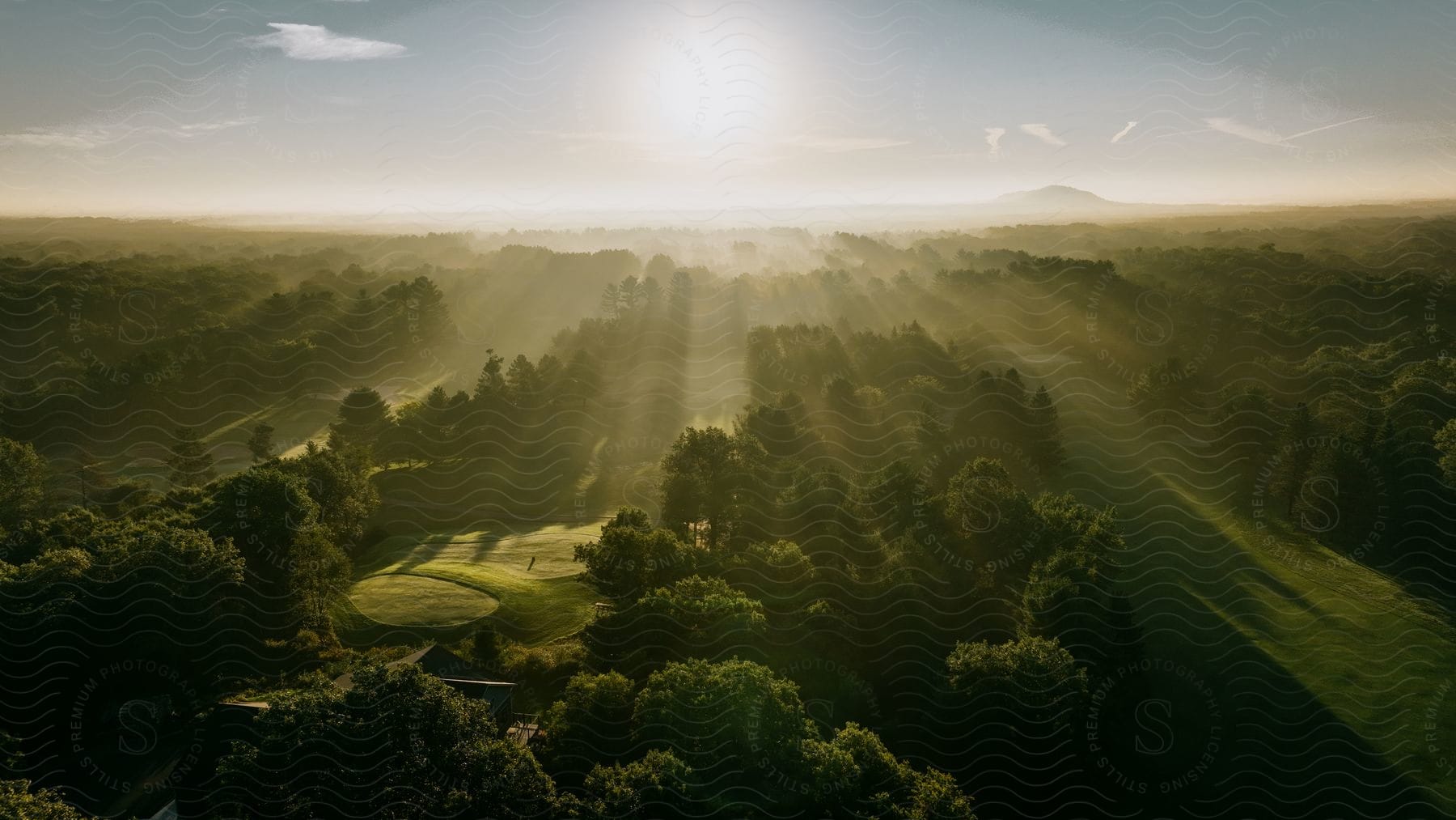 Aerial view of a green golf course with the sun shining over it