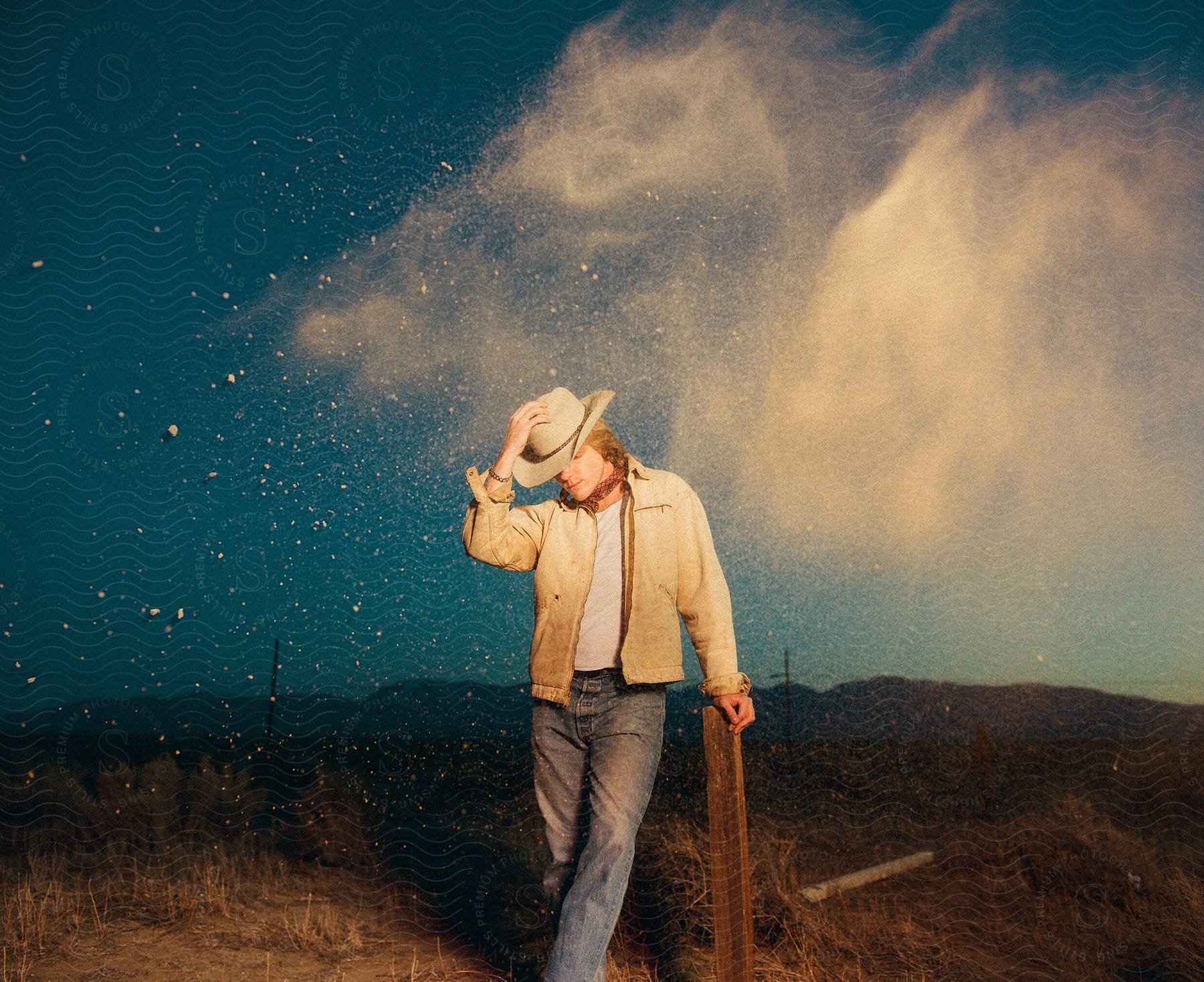 Stock photo of a man in a cowboy hat poses on the grasslands while dirt is thrown in the air