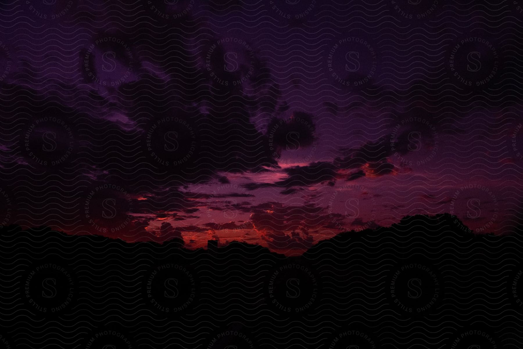 Hilly terrain silhouetted against a purple sunset sky