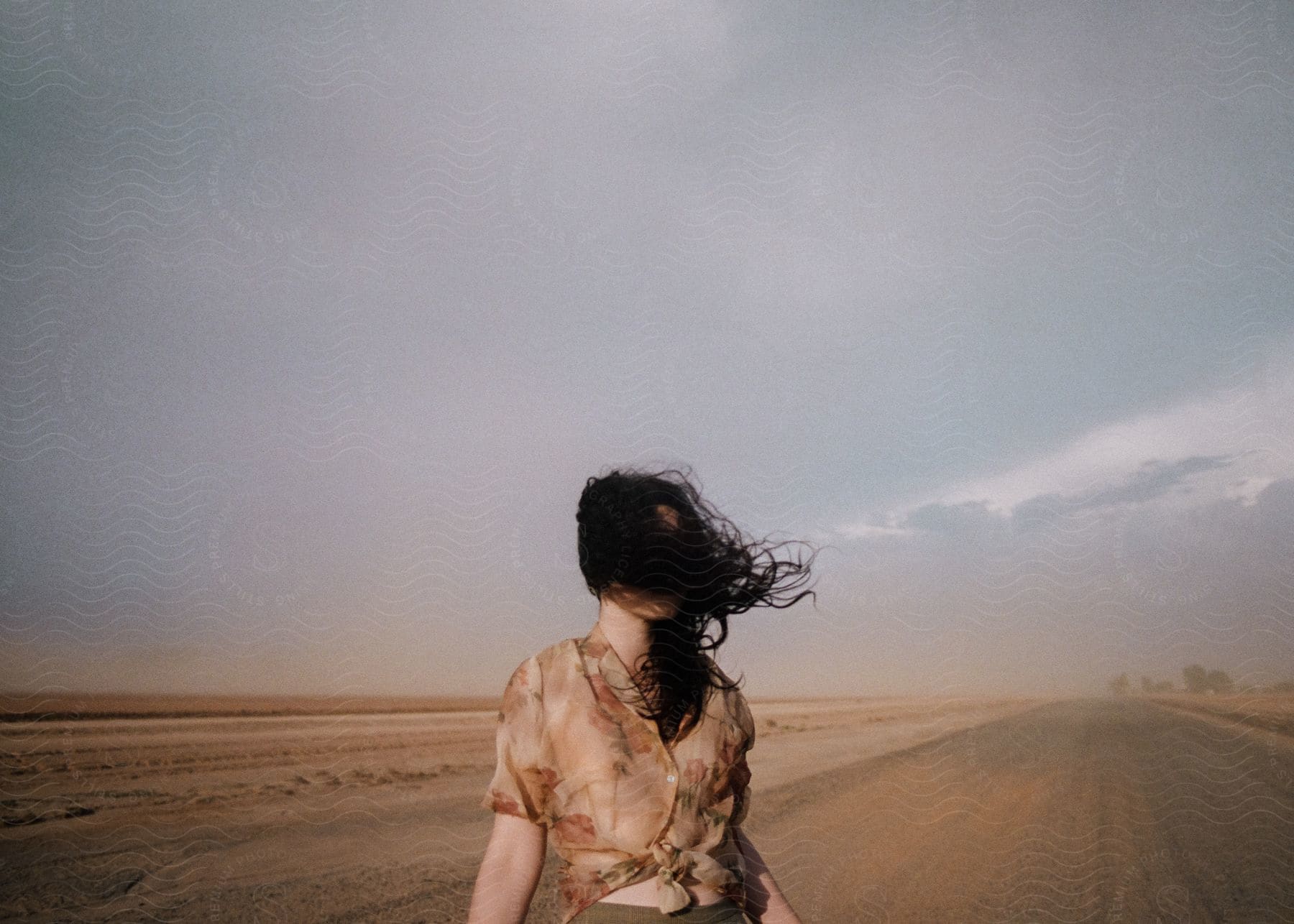 A happy woman with black hair and a blouse standing outdoors with the sky and horizon in the background