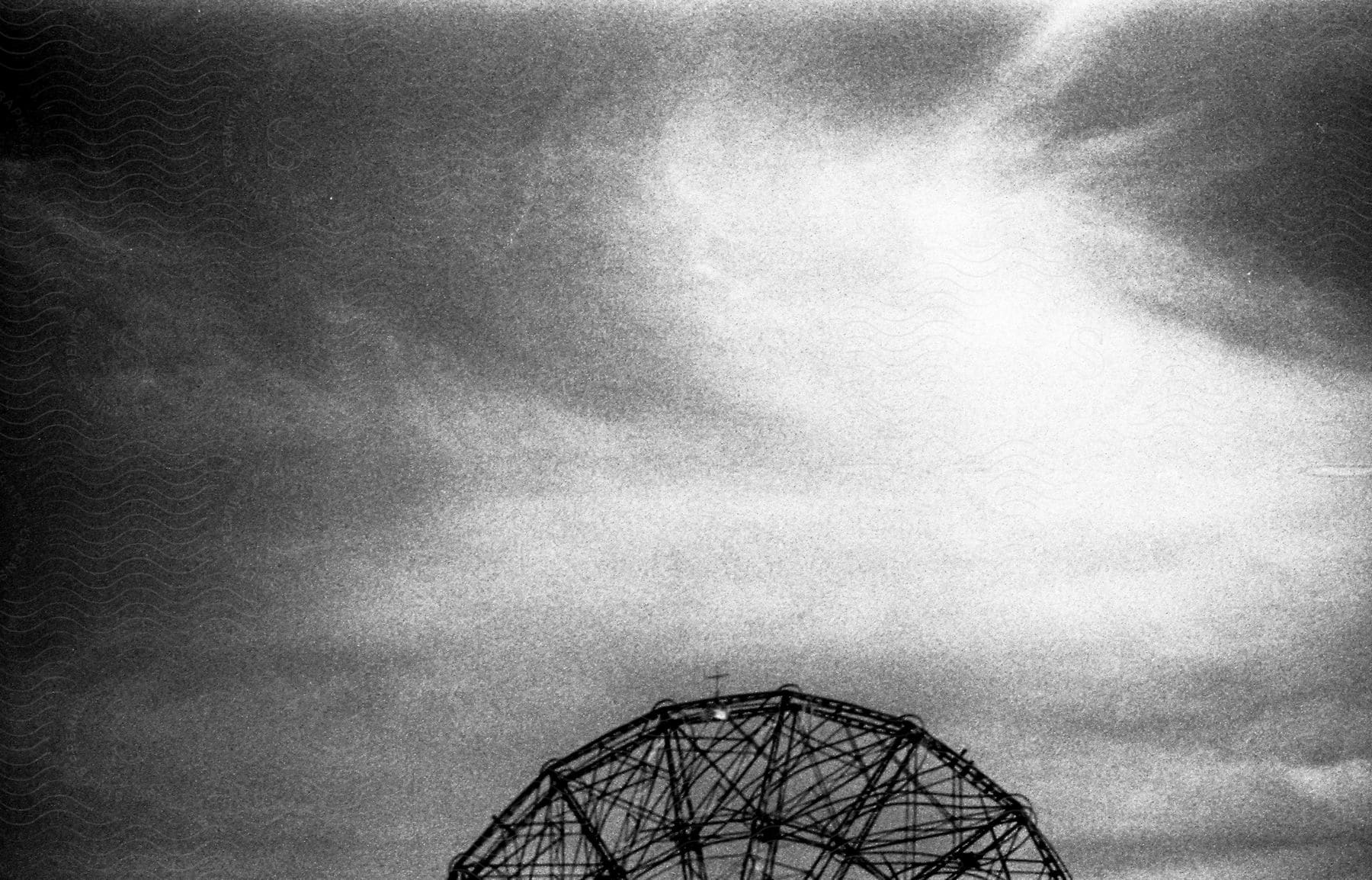 Black and white shot of a ferris wheel under clouds at coney island