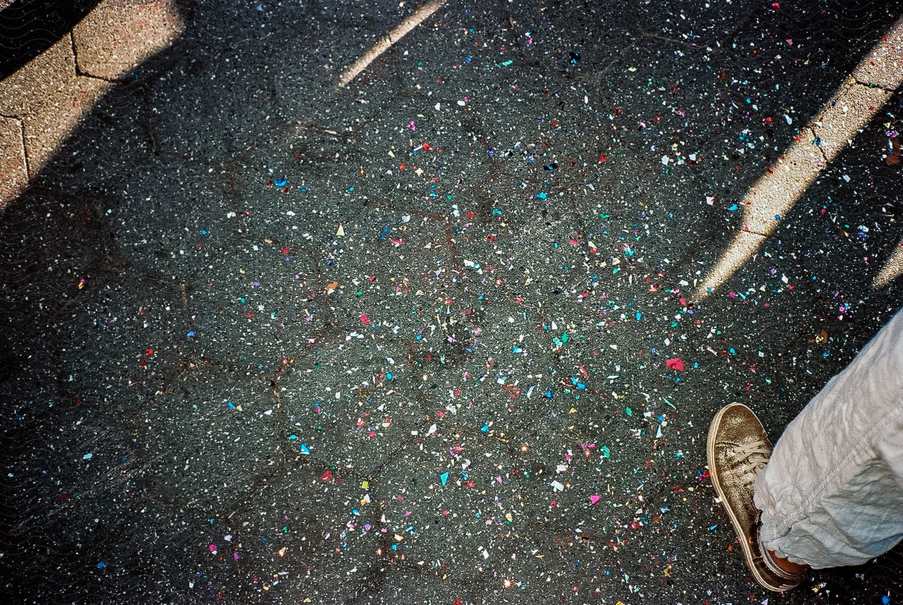 Brightly colored flecks on asphalt a persons leg at the edge of the photo