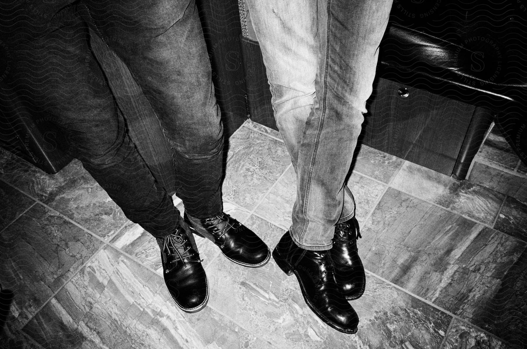 Two men standing with their feet on a grey floor wearing jeans and shoes