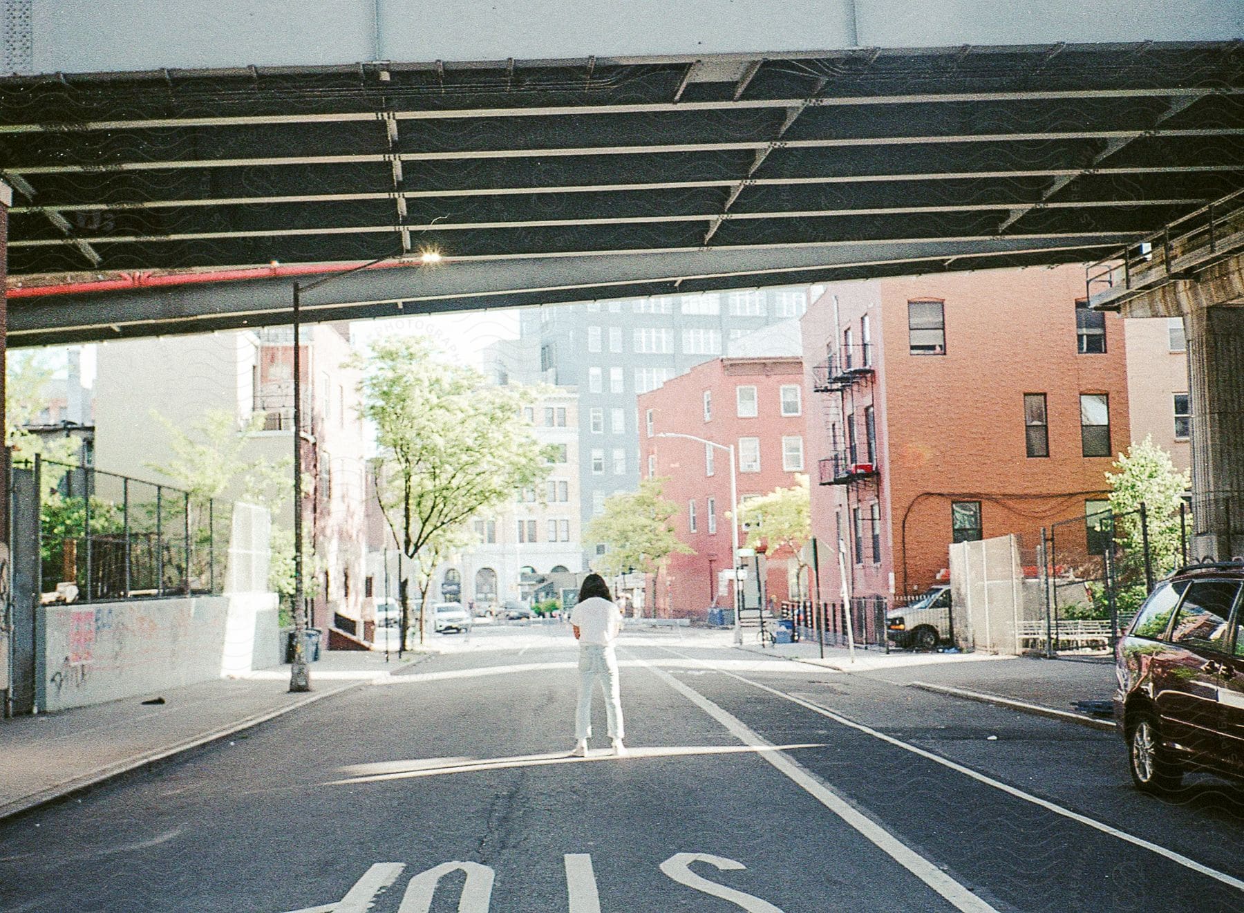 Woman with dark hair white tshirt and jeans stands in the middle of road under overpass in nyc