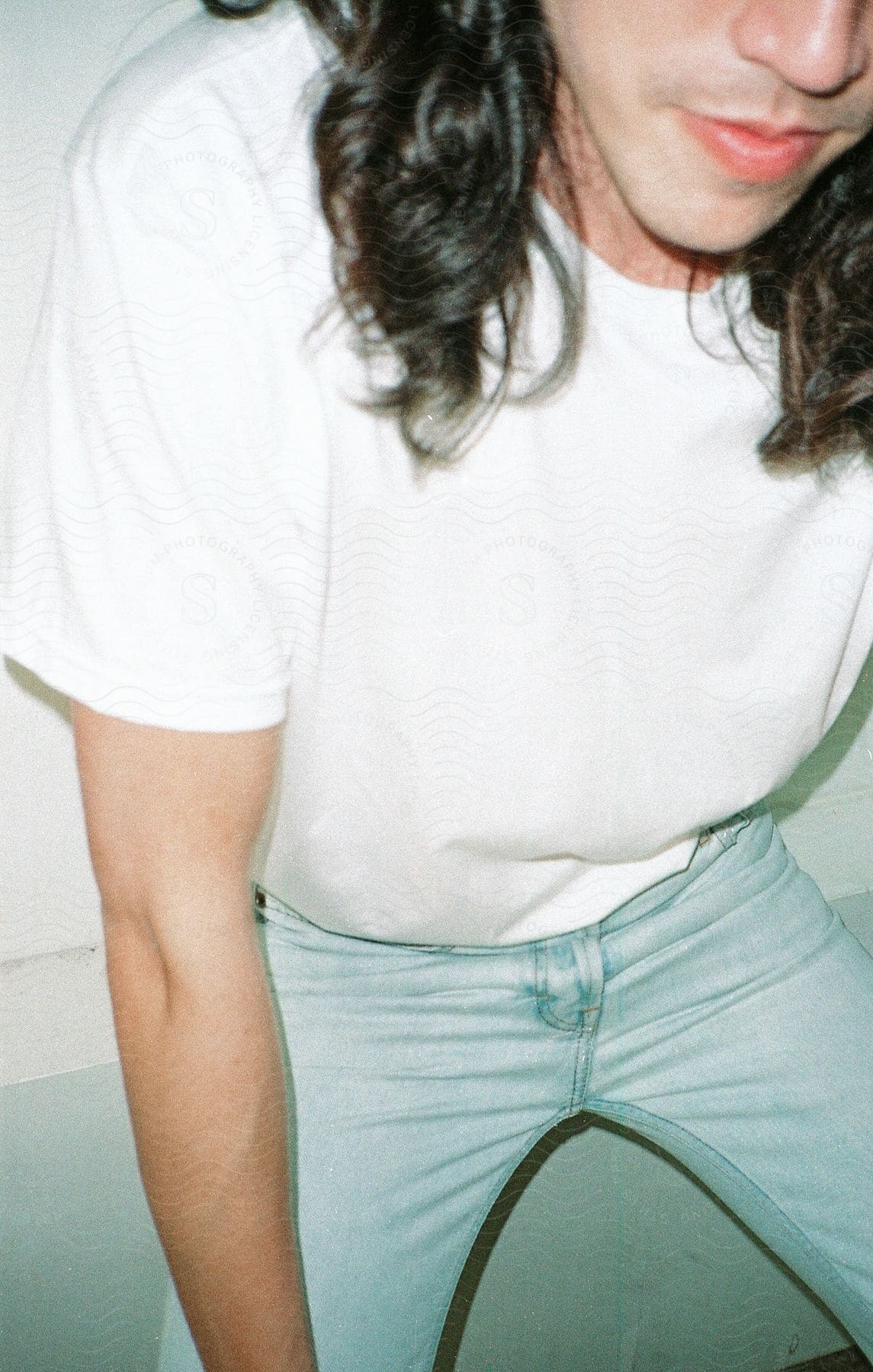 Man crouching down wearing a white shirt and jeans with long hair