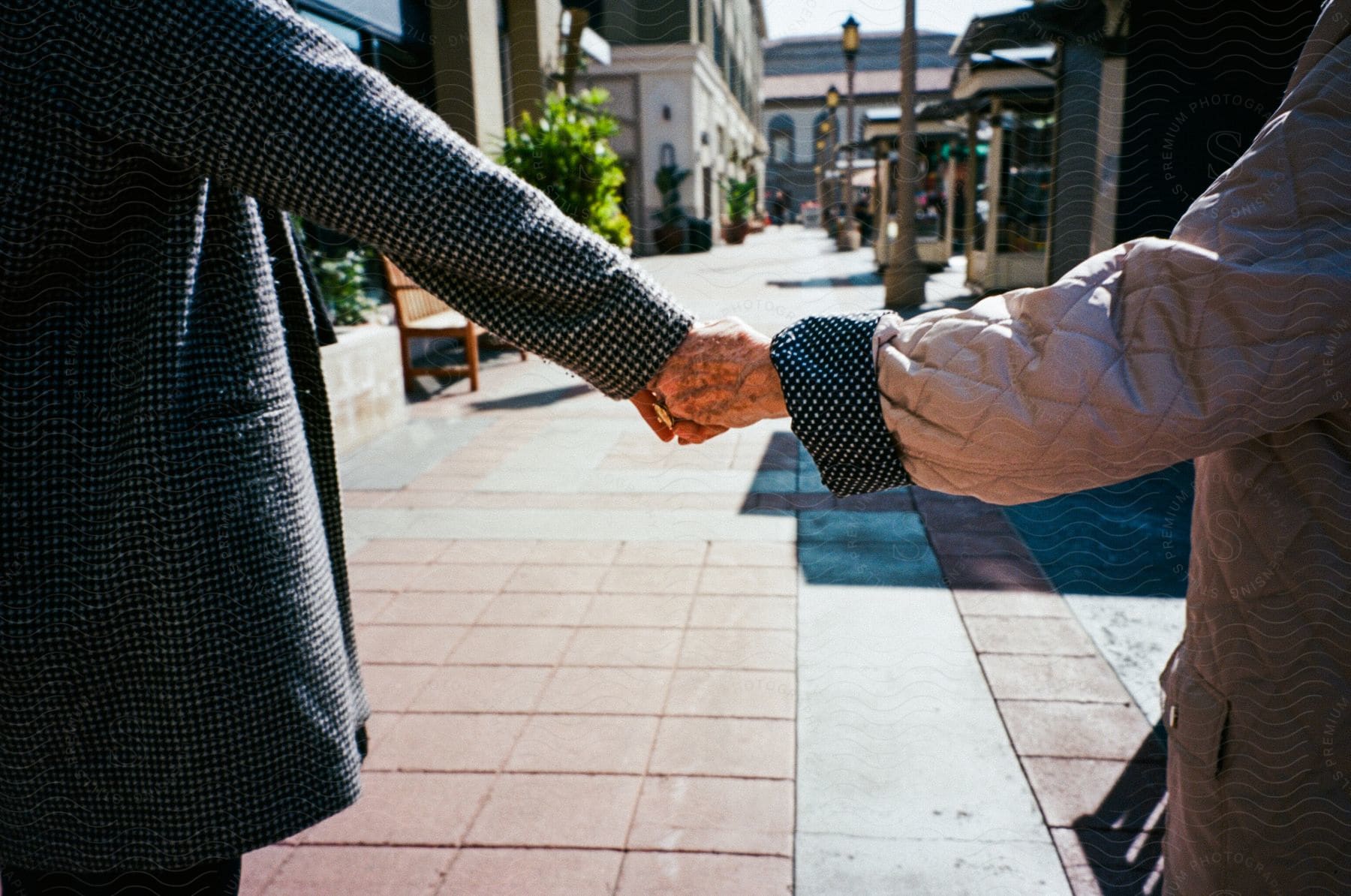 Elderly couple holding hands while walking on a sidewalk between shops