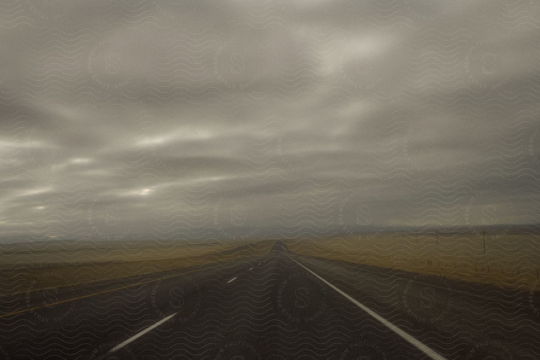 An empty highway runs through untouched flat grassland under a dark cloudy sky