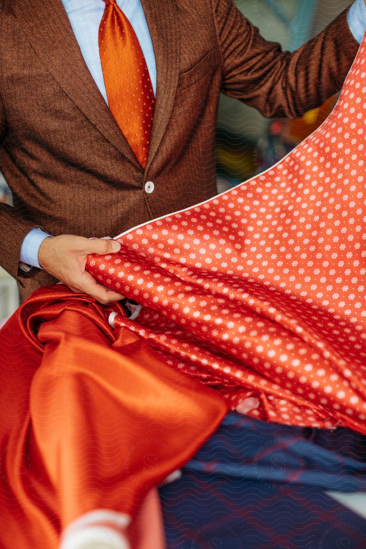 A man in a brown suit holds orange polka dot fabric