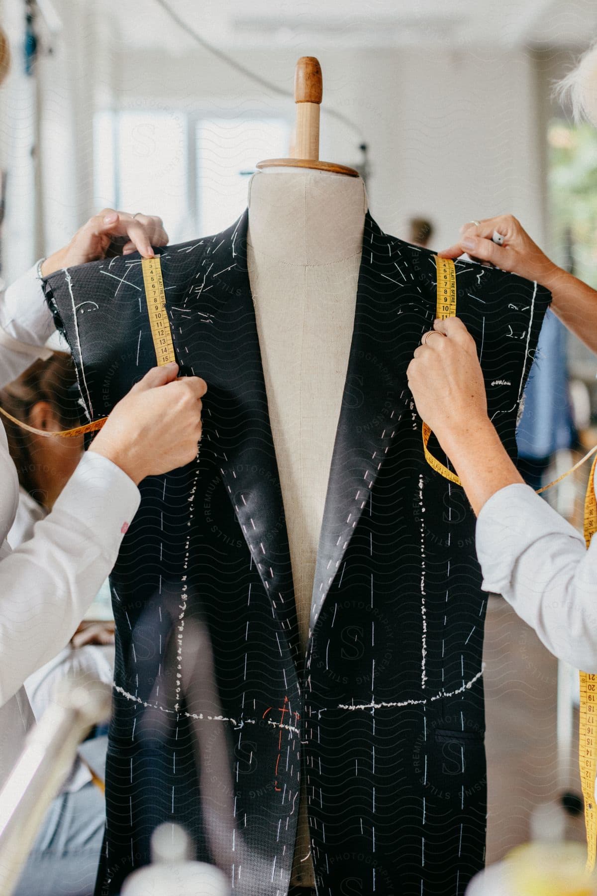 Stock photo of two persons measuring the shoulder of a black and white striped jacket in an interior setting