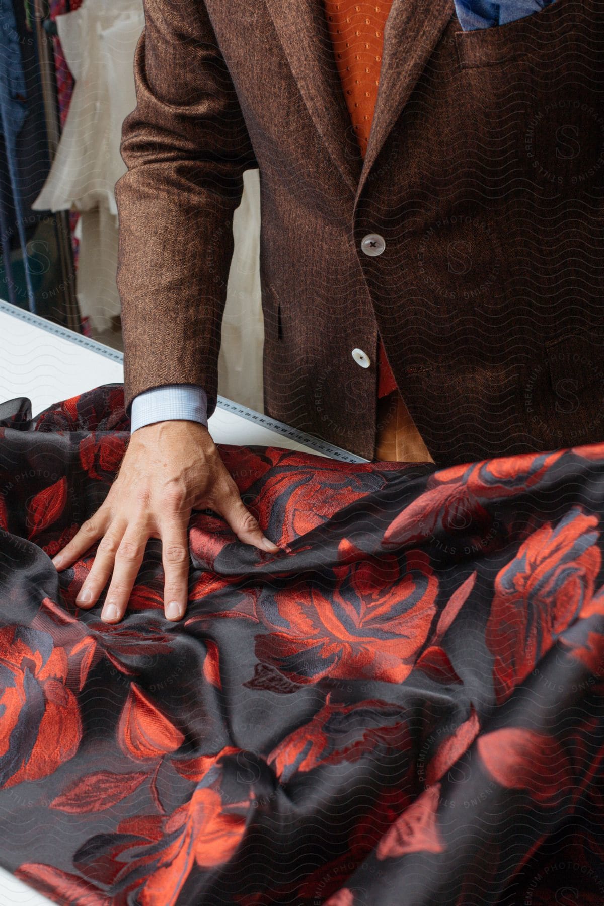 A man in a brown suit coat and orange tie examines a red and black floral print fabric