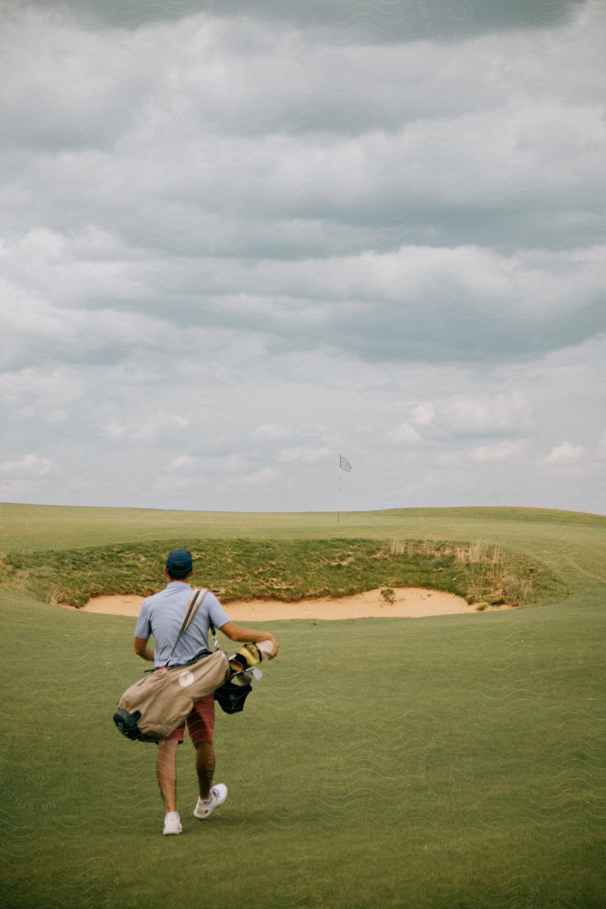 Man walking along green carrying golf bag on an overcast day at a golf course