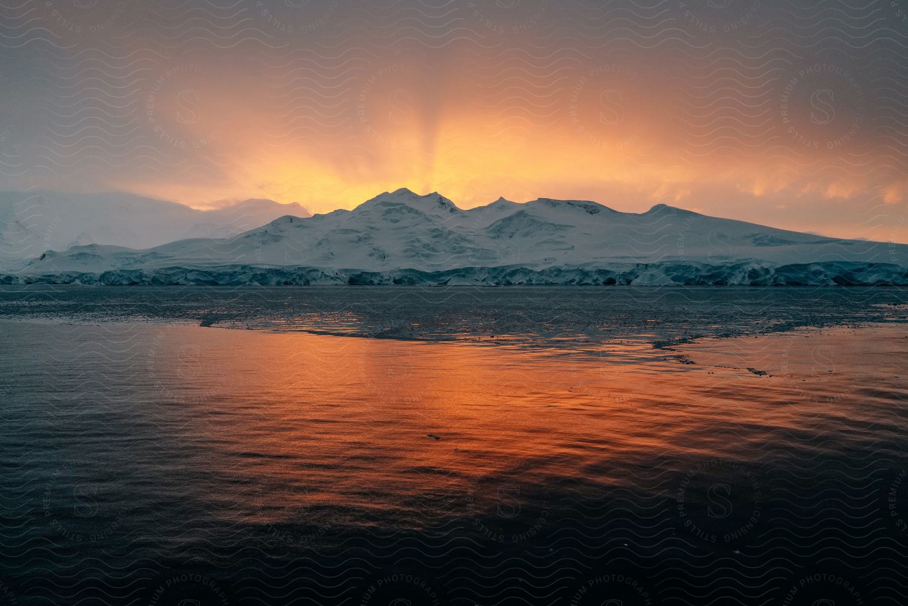 Snowy mountain near serene lake at sunset in antarctica