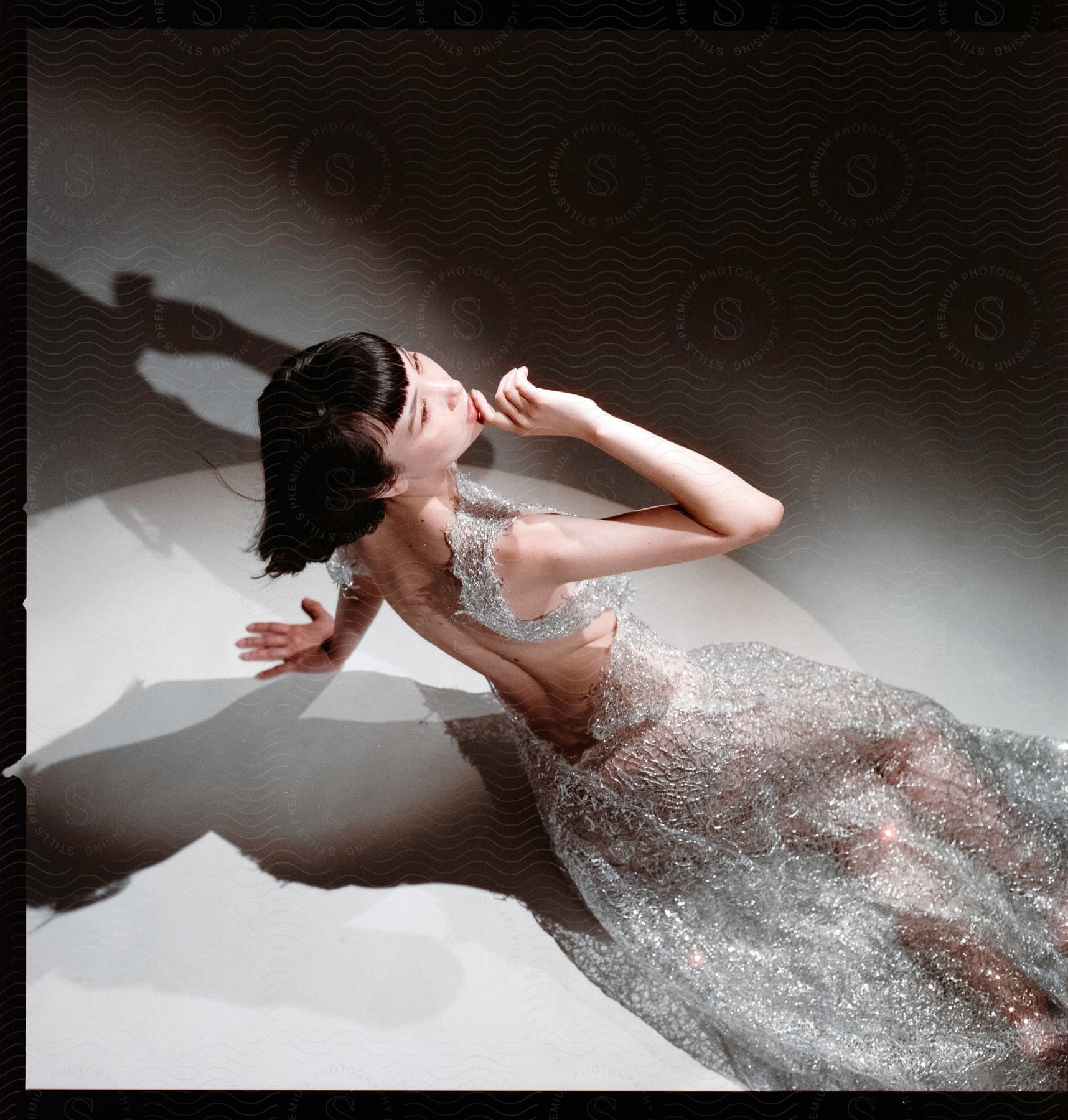 An asian model posing on a white table in a shimmery but slightly see through dress