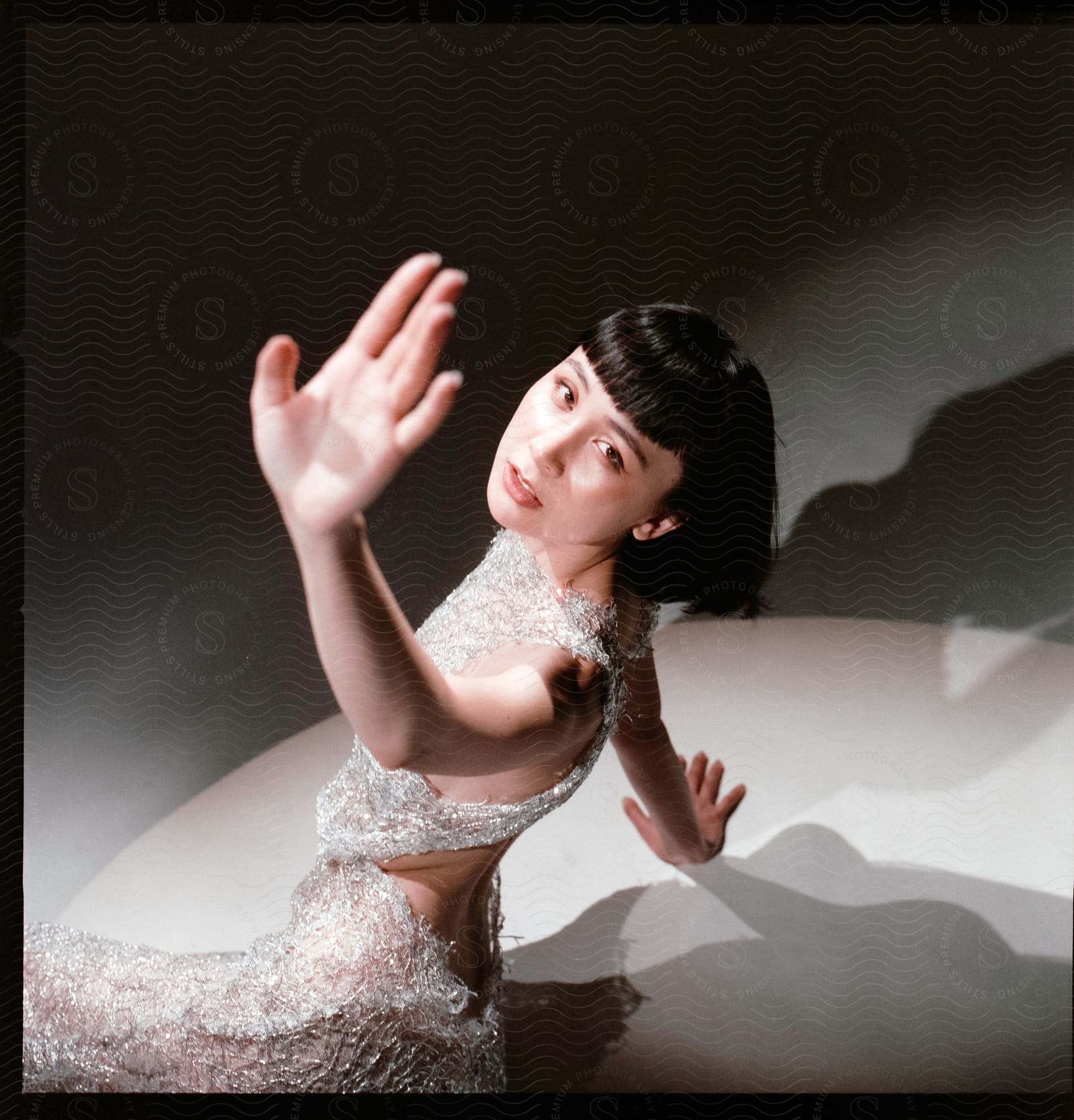 Model in shimmering dress with hand raised blocking light above