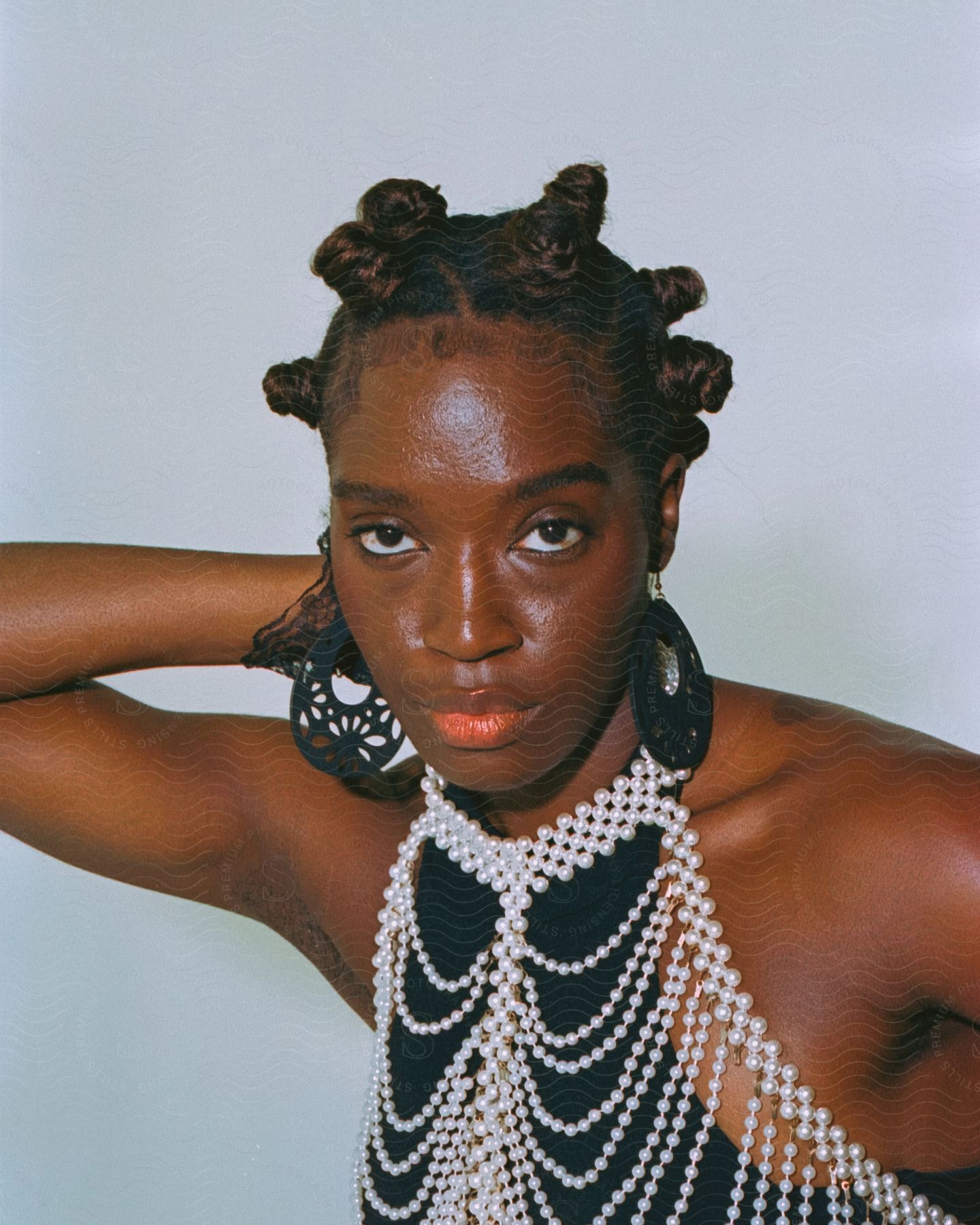 A young woman wearing jewelry looks directly at the camera in closeup