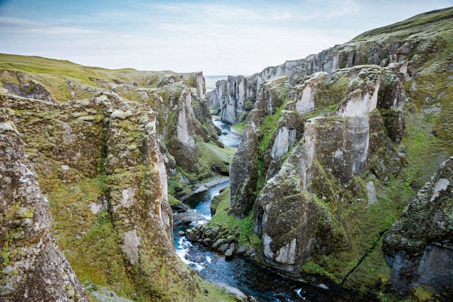 A serene landscape of a mountainous region with a flowing watercourse and grassy terrain under a cloudy sky