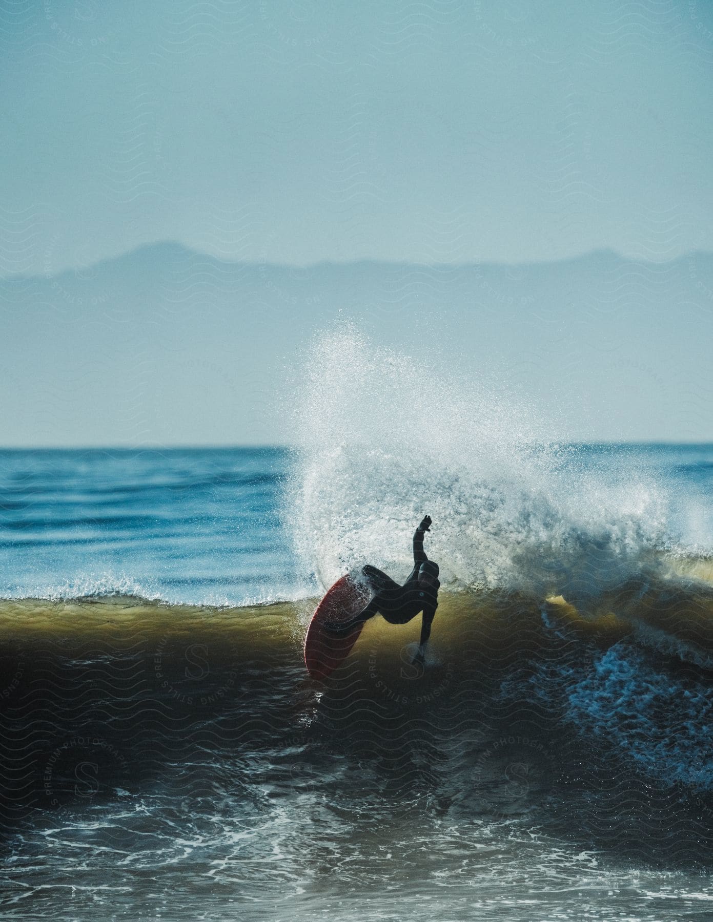 A determined man surfing a wave with mountains in the background