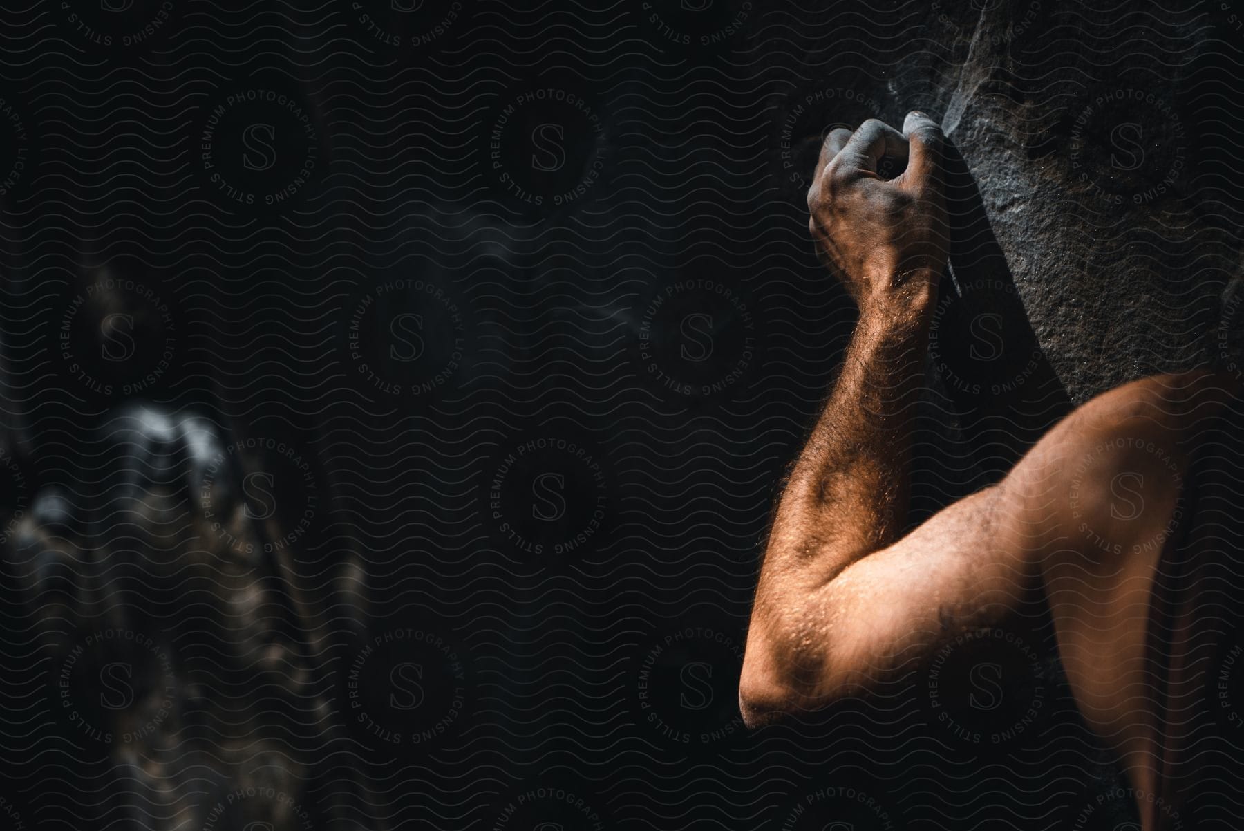 A determined adult male rock climber with freshly coated fingers attempts to navigate a cavernous rock formation