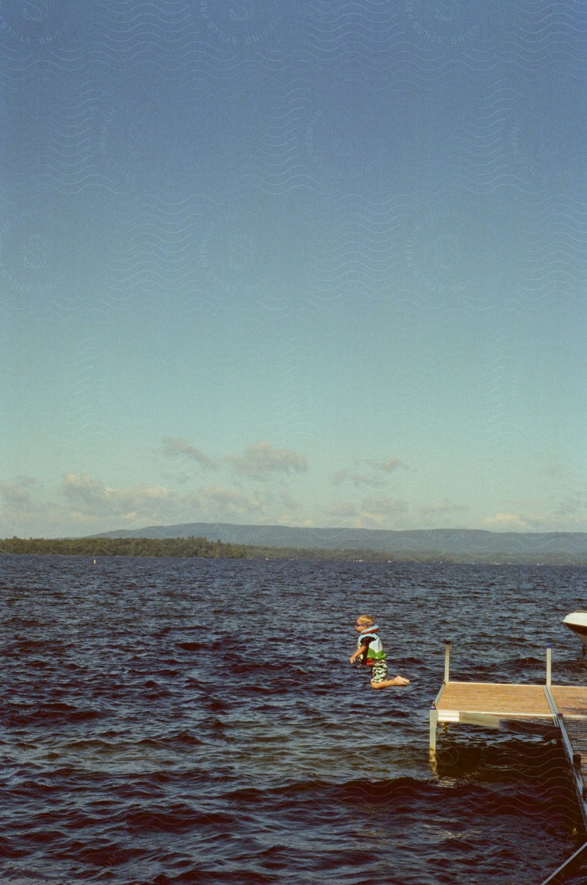 A boy jumps off a pier into a lake wearing a life jacket