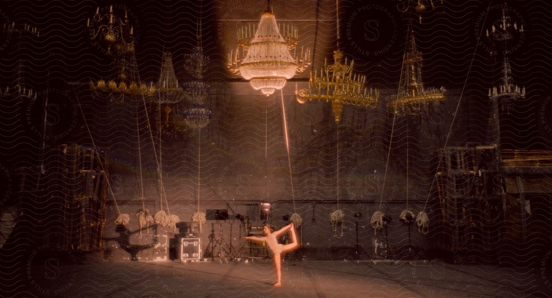 A female ballet dancer performs alone in a theater surrounded by chandeliers and other props