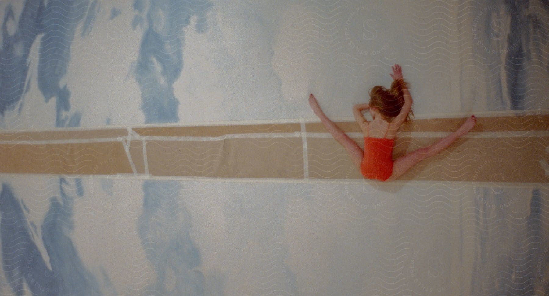 Female ballet dancer lying on parchment paper on a sky mural spreading her legs to form a v