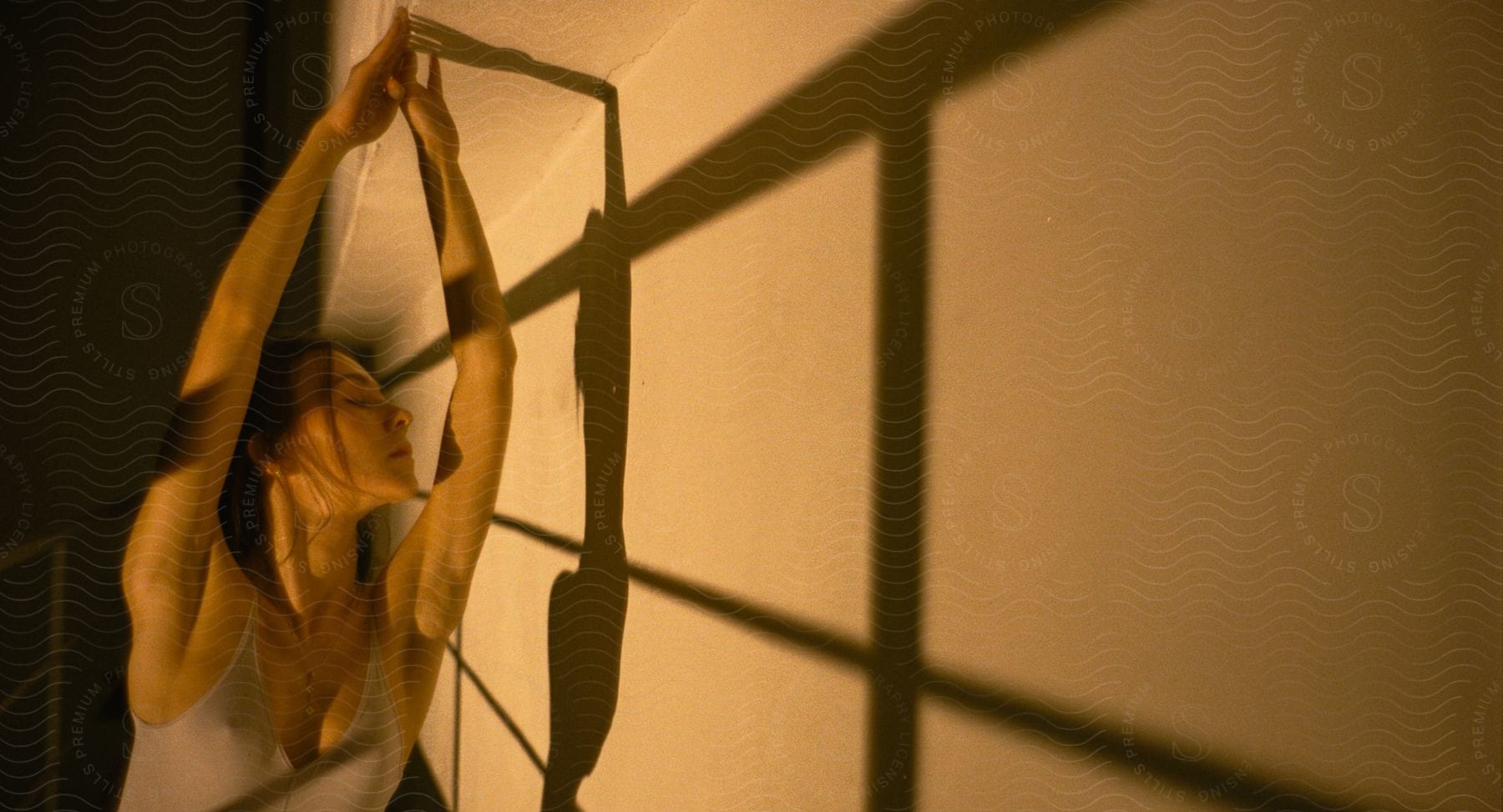 A ballet dancer with closed eyes and raised hands touching a wall in a theater