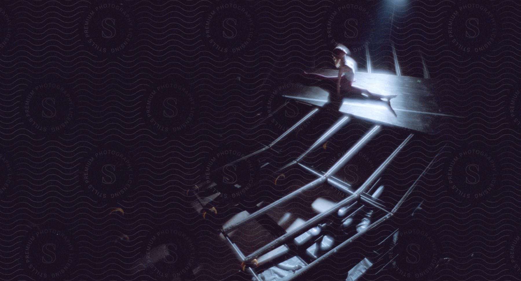 A ballet dancer performs a front split on a narrow platform in a theater