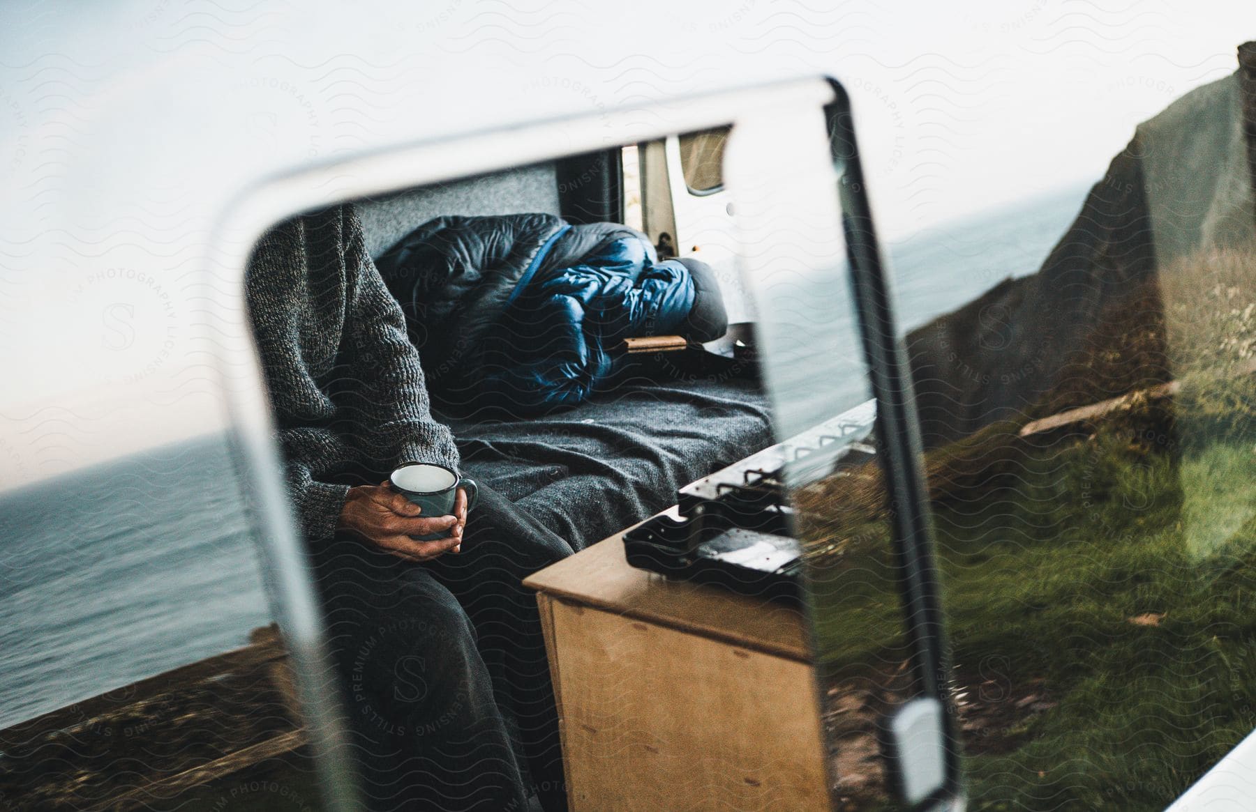 A person sitting and holding a cup looking at the ocean