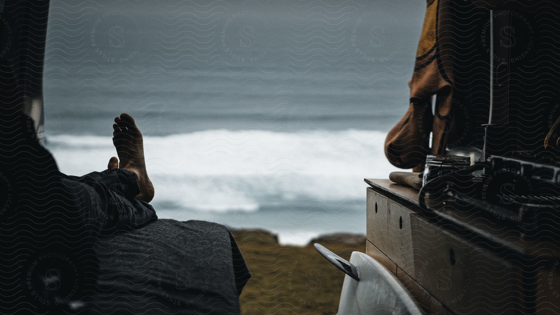 A man sits on a bed inside a tent facing the sea