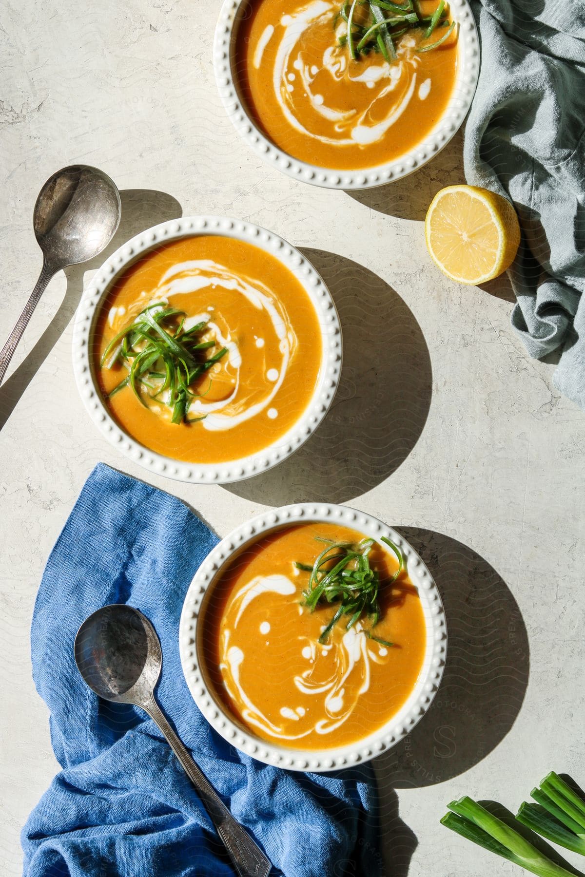 Three bowls of orange soup with lemon and spoons surrounding the bowls